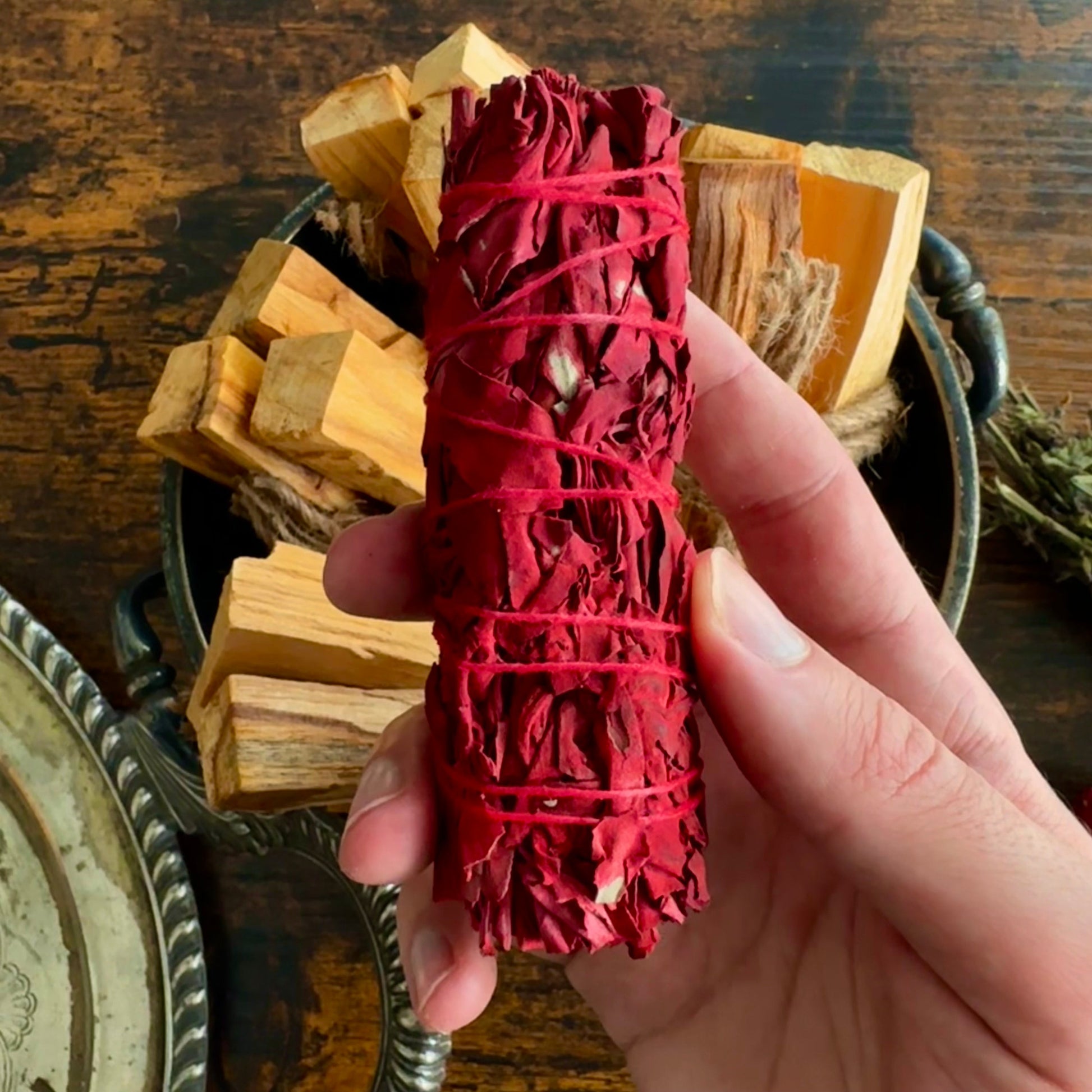 Hand holding a red smudge stick with wooden blocks and a mirror in the background.