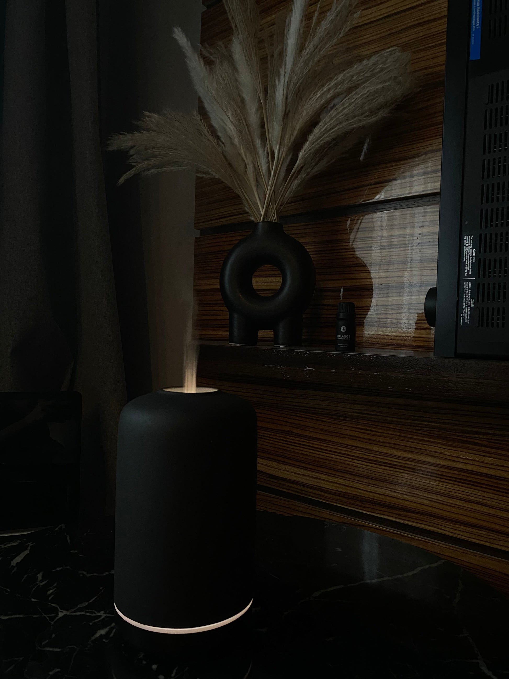 ash essential oil diffuser aromatherapy home decor with dried plants on a wooden shelf in a dimly lit room