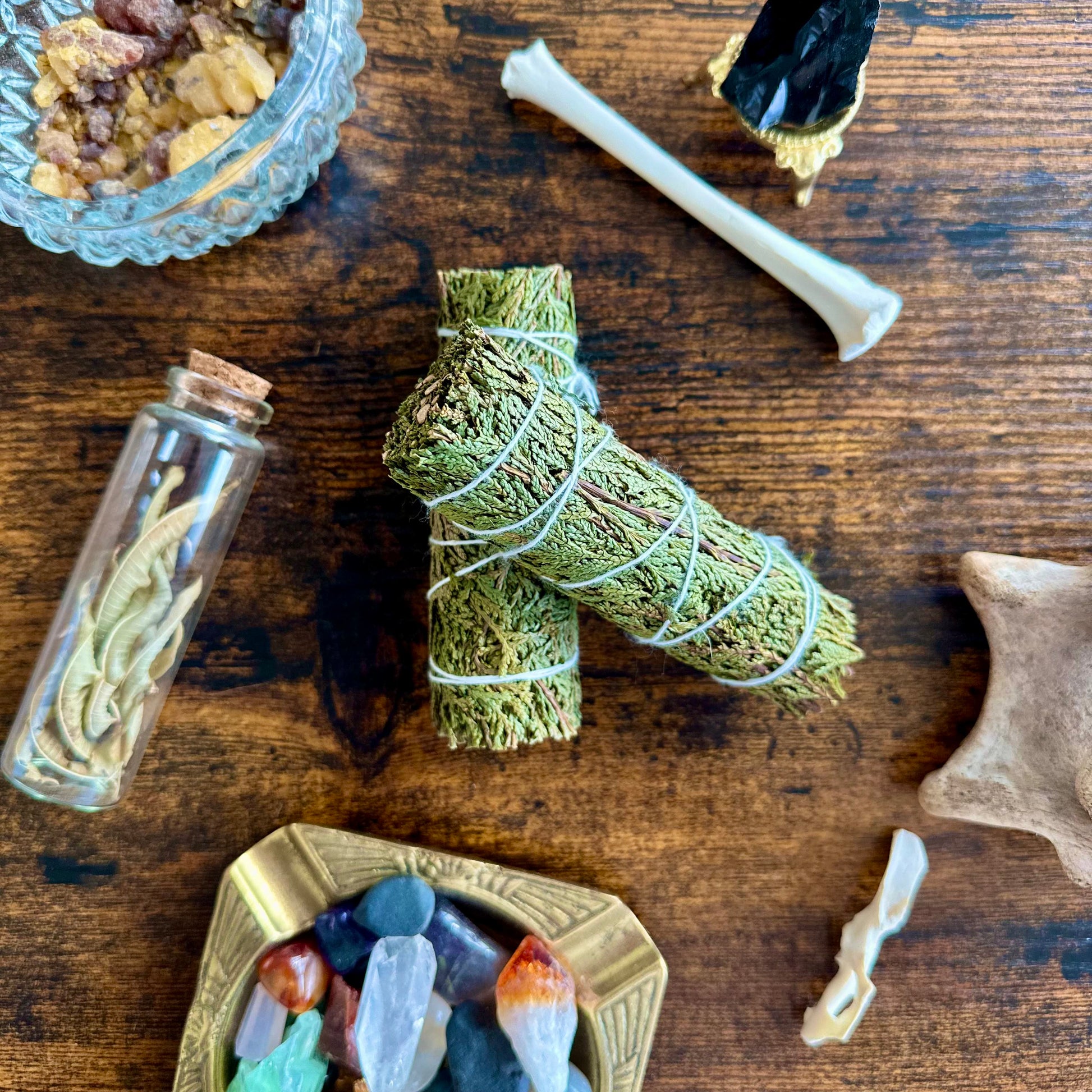 cedar sage surrounded by herbal bundle, crystal bowl, and other items on a wooden surface