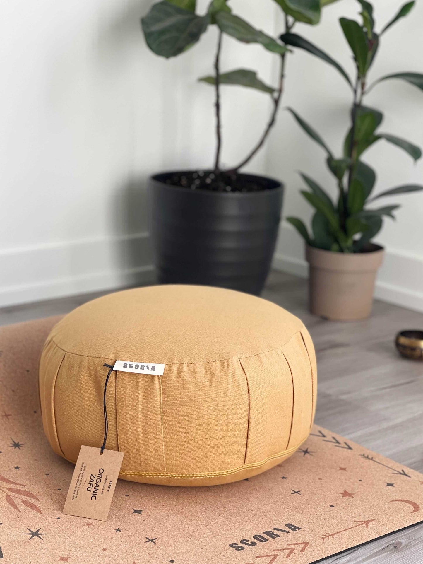gold meditation cushion with a tag on a cork mat, plants in the background
