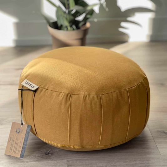 Round mustard-colored ottoman on a wooden floor with a plant in the background