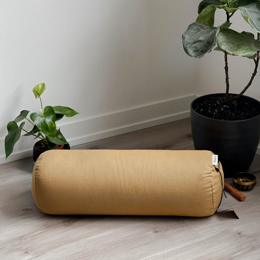 gold yoga bolster on a floor with some plants