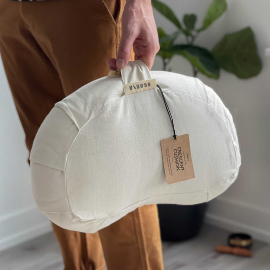 Person holding a cloud-shaped yoga cushion with a visible brand tag indoors.