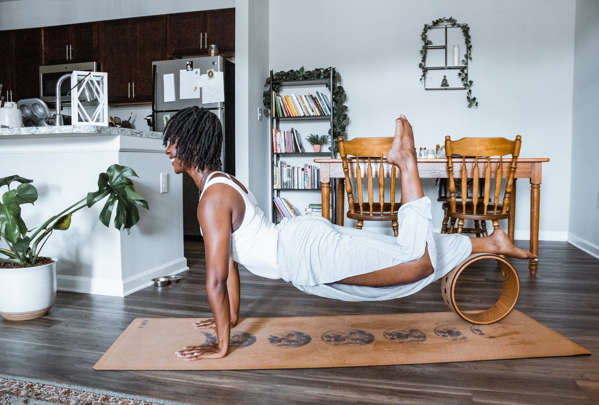 Person doing a yoga pose on a Cork yoga mat with moon phase design and wheel in a home setting