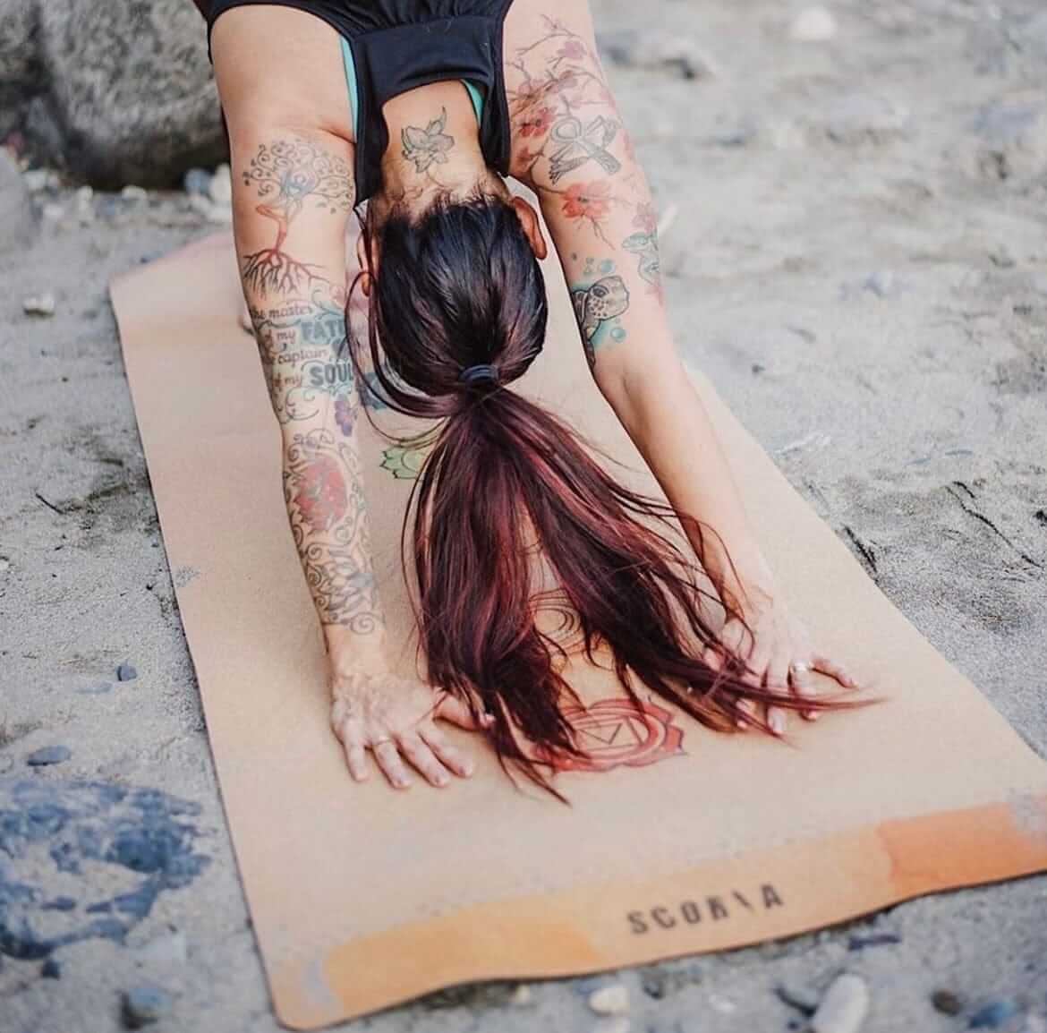 Person doing a handstand on a Cork yoga mat with chakra symbols on a sandy surface.