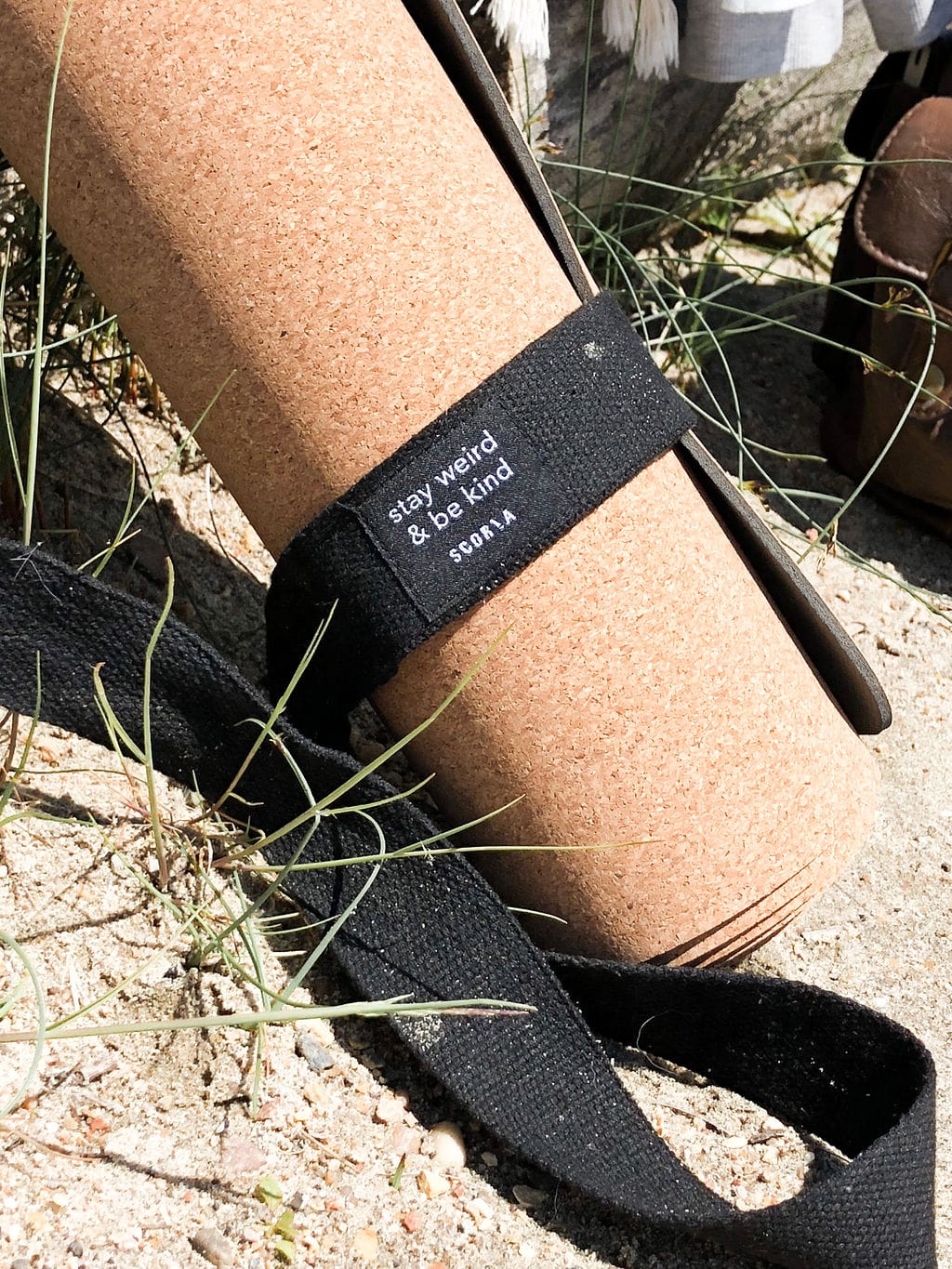 Cork yoga mat with a black strap labeled 'stay weird & be kind' on a natural background.