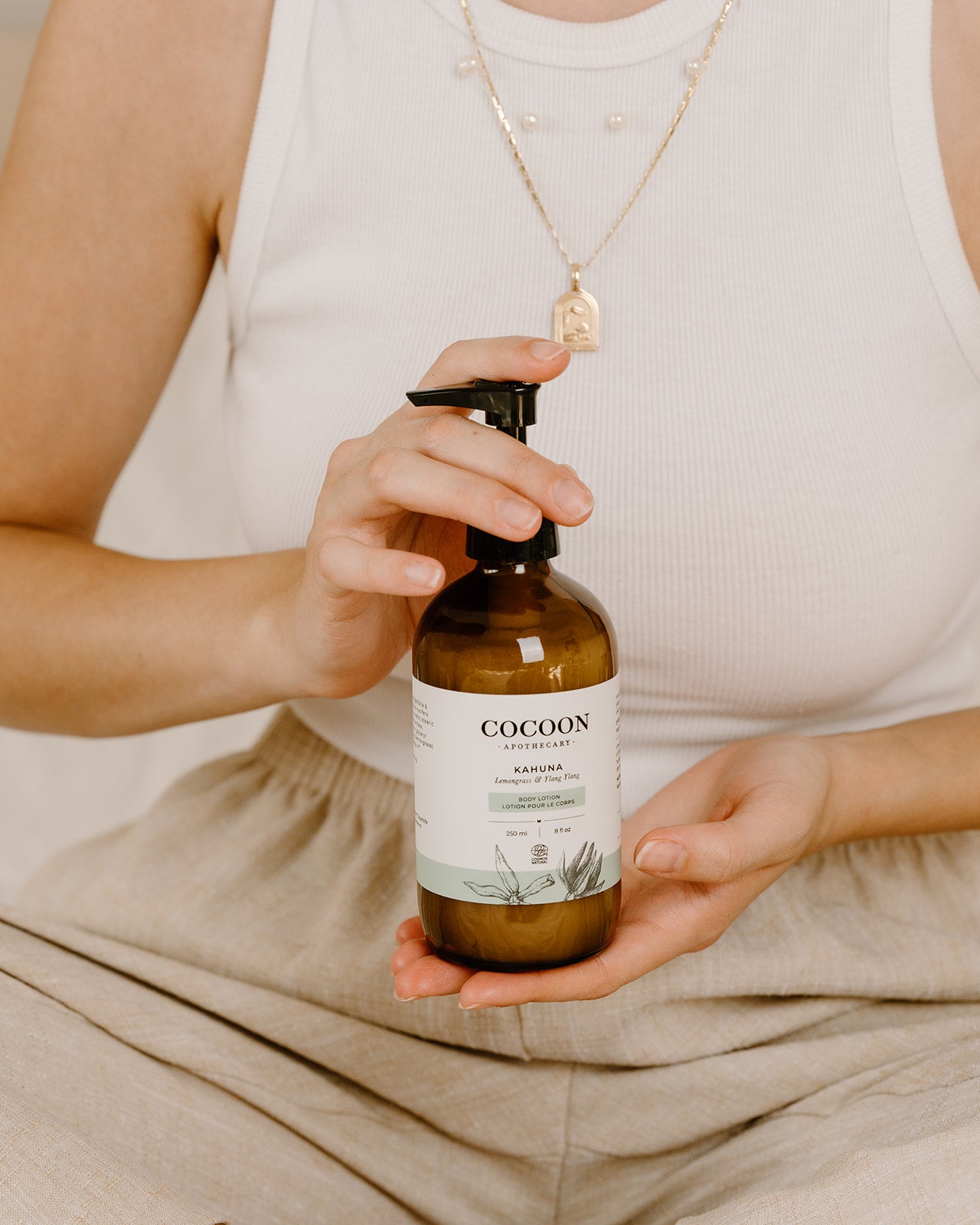 Person holding a bottle of 'Cocoon' body lotion with a neutral background