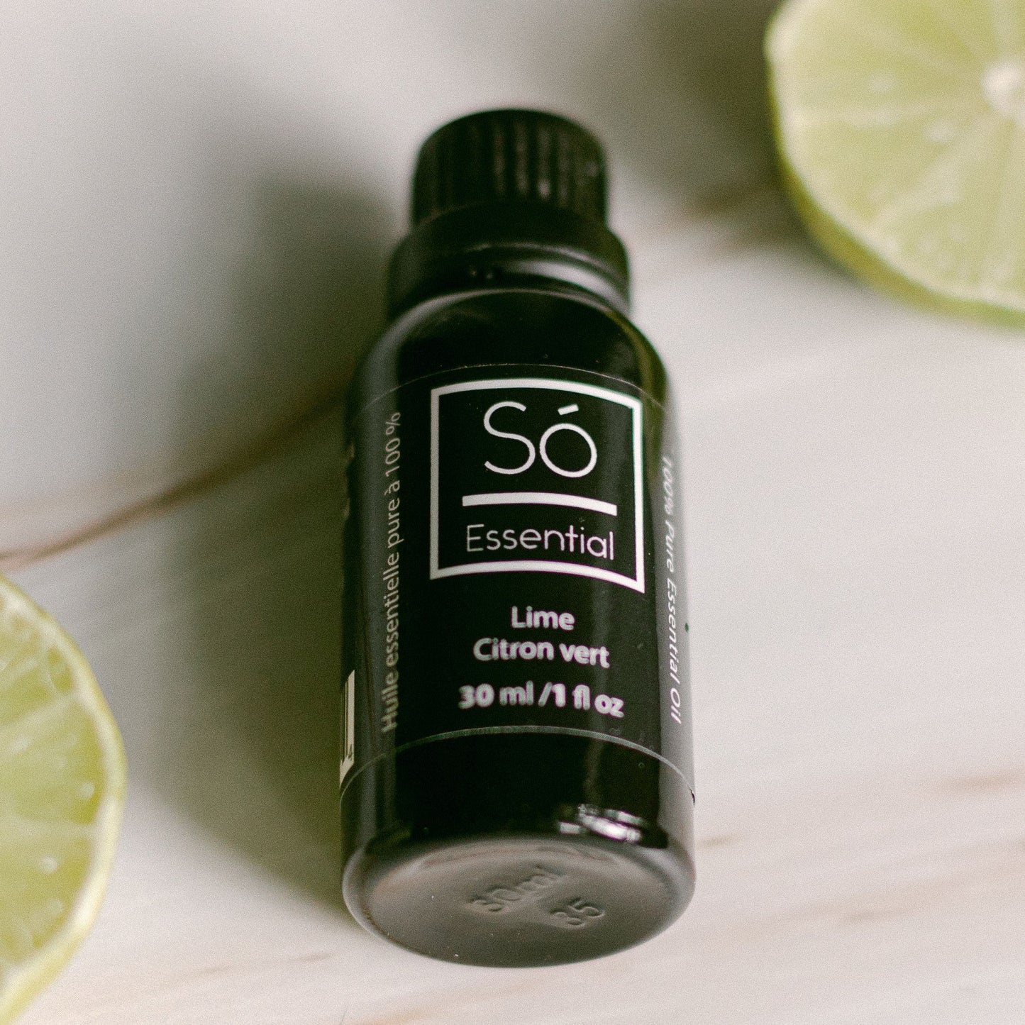 Lime essential oil bottle labeled 'Sö Essential' with lime slices on a light surface