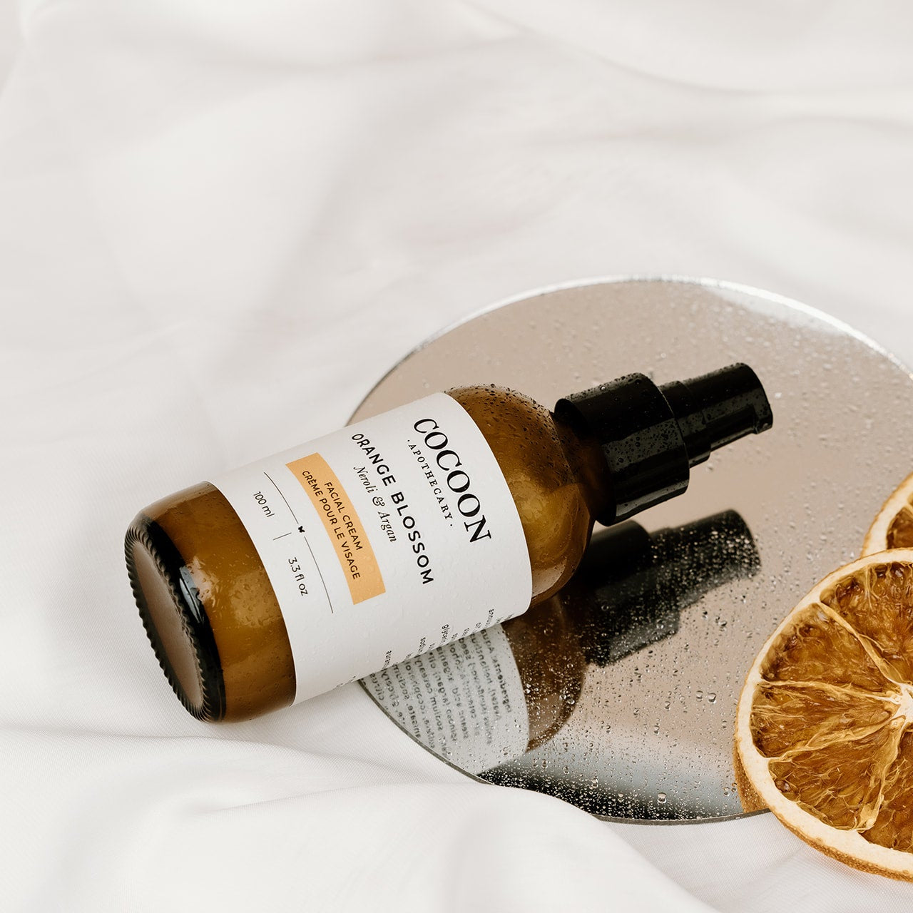 facial skincare bottle with a dropper on a reflective surface with dried oranges.