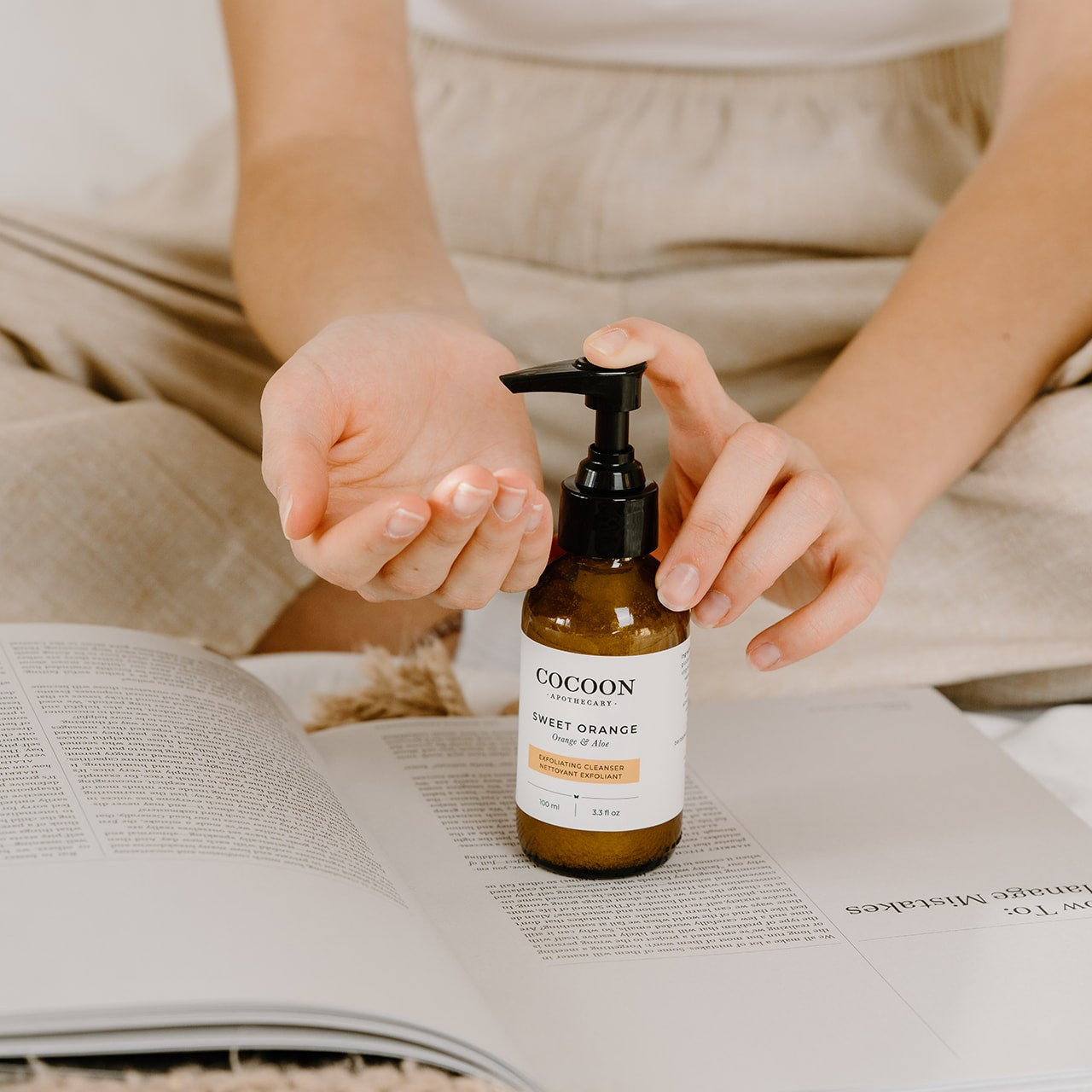 Person holding a bottle of Cocoon Sweet Orange facial cleanser on an open book.