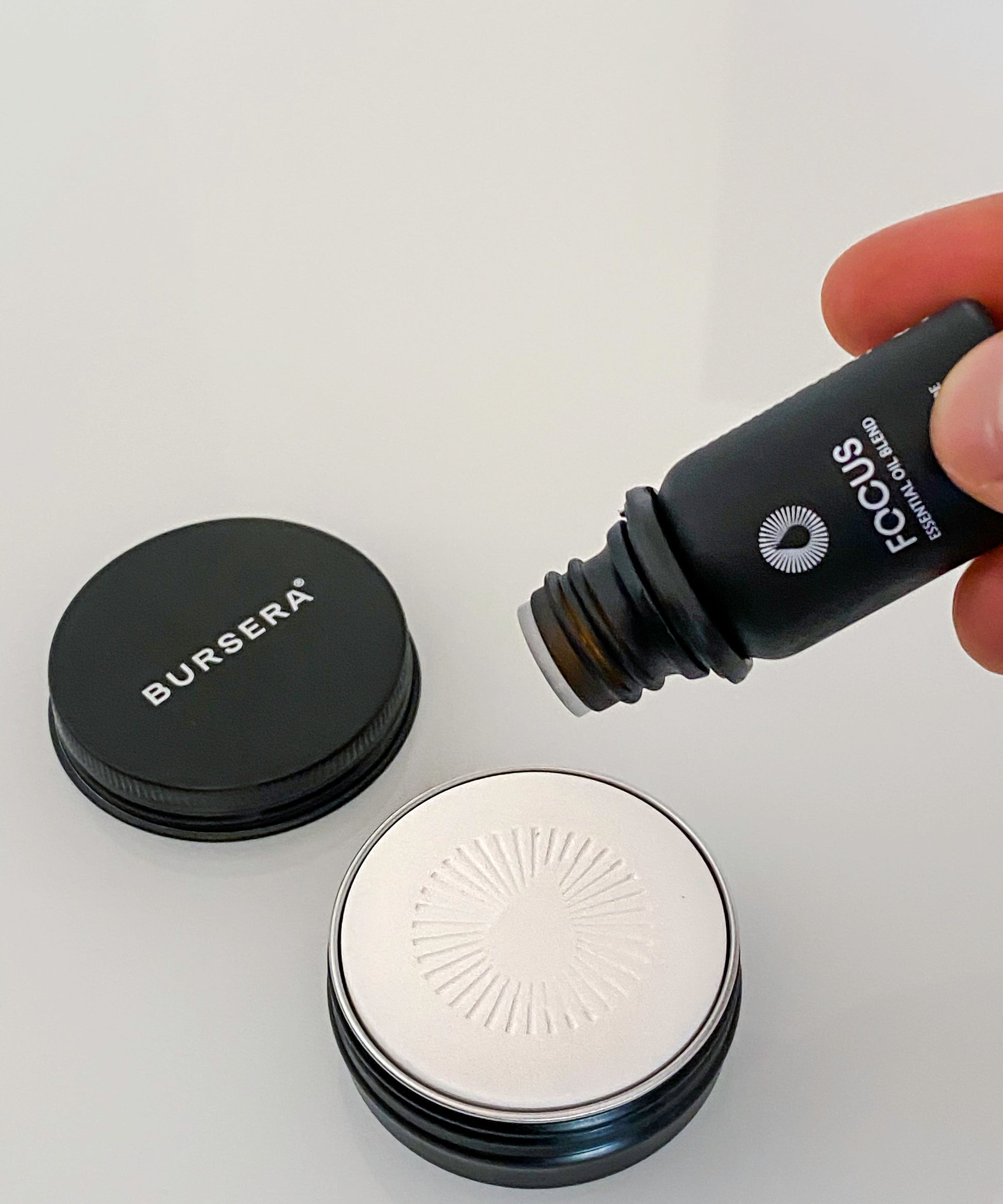 Person pouring a product from a Bursera bottle onto diffusing stone essential oil aromatherapy decor with a gray background