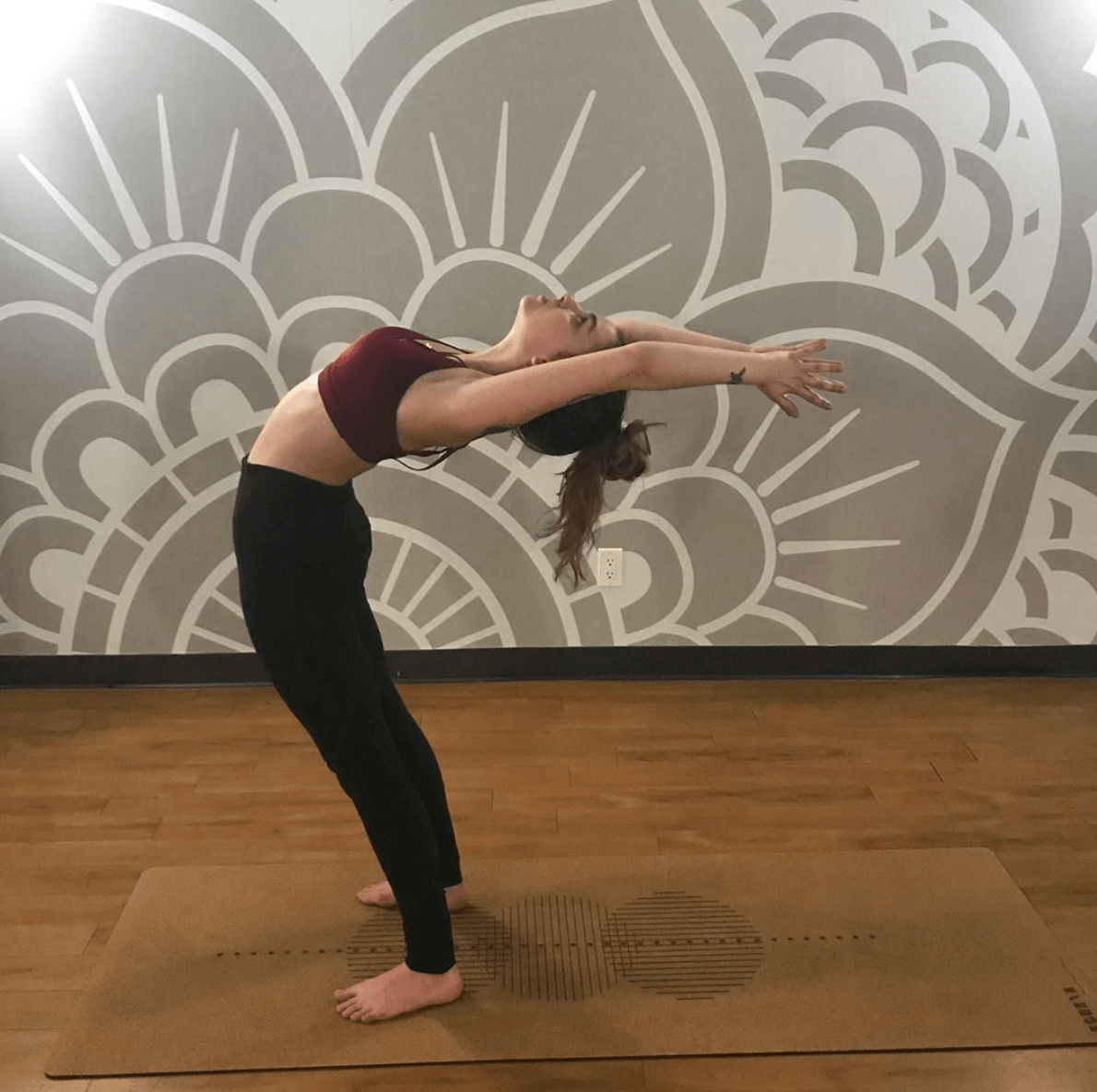 Person practicing yoga on a geometric cork yoga mat in a studio with a patterned wall.