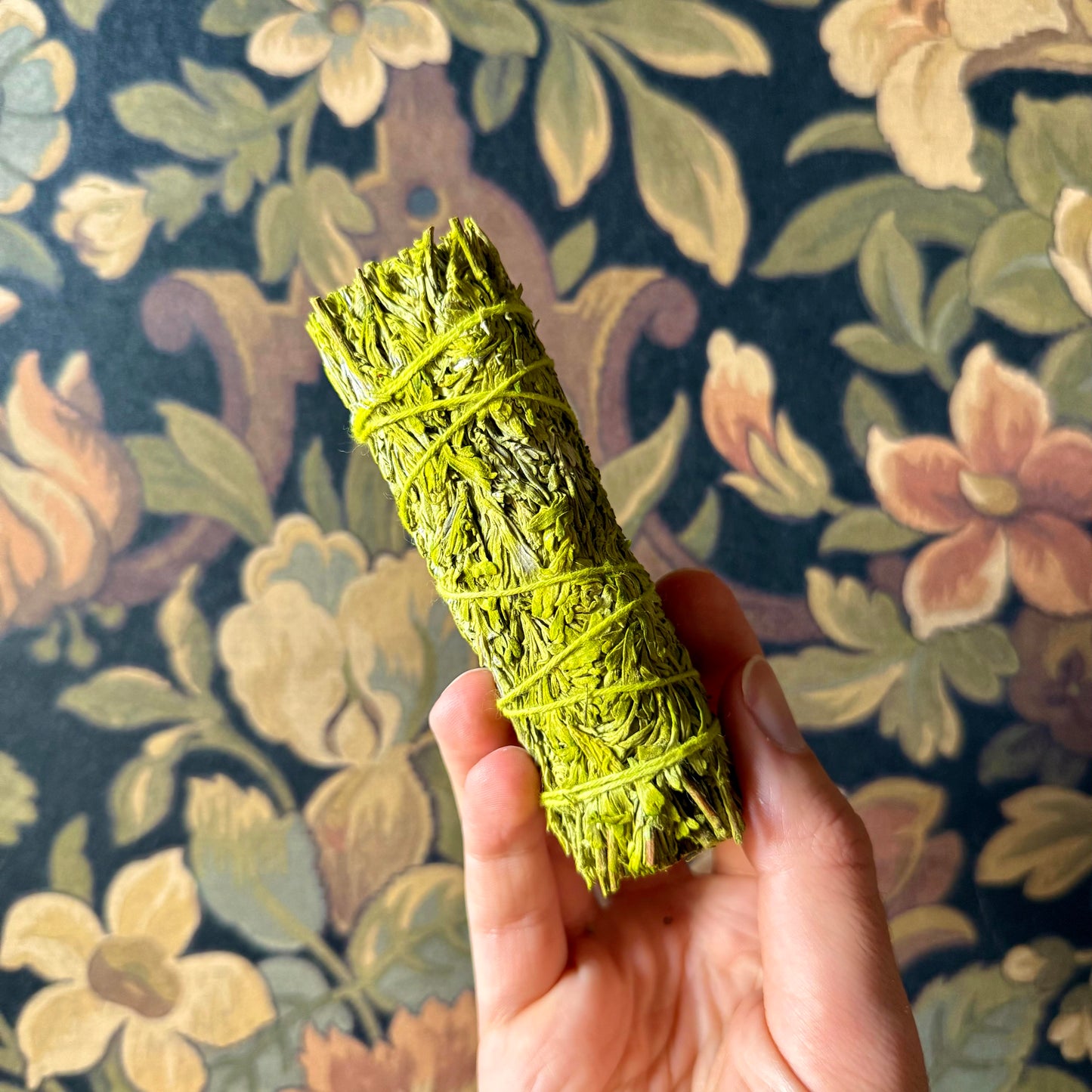 Hand holding a bundle of green patchouli sage against a floral-patterned background