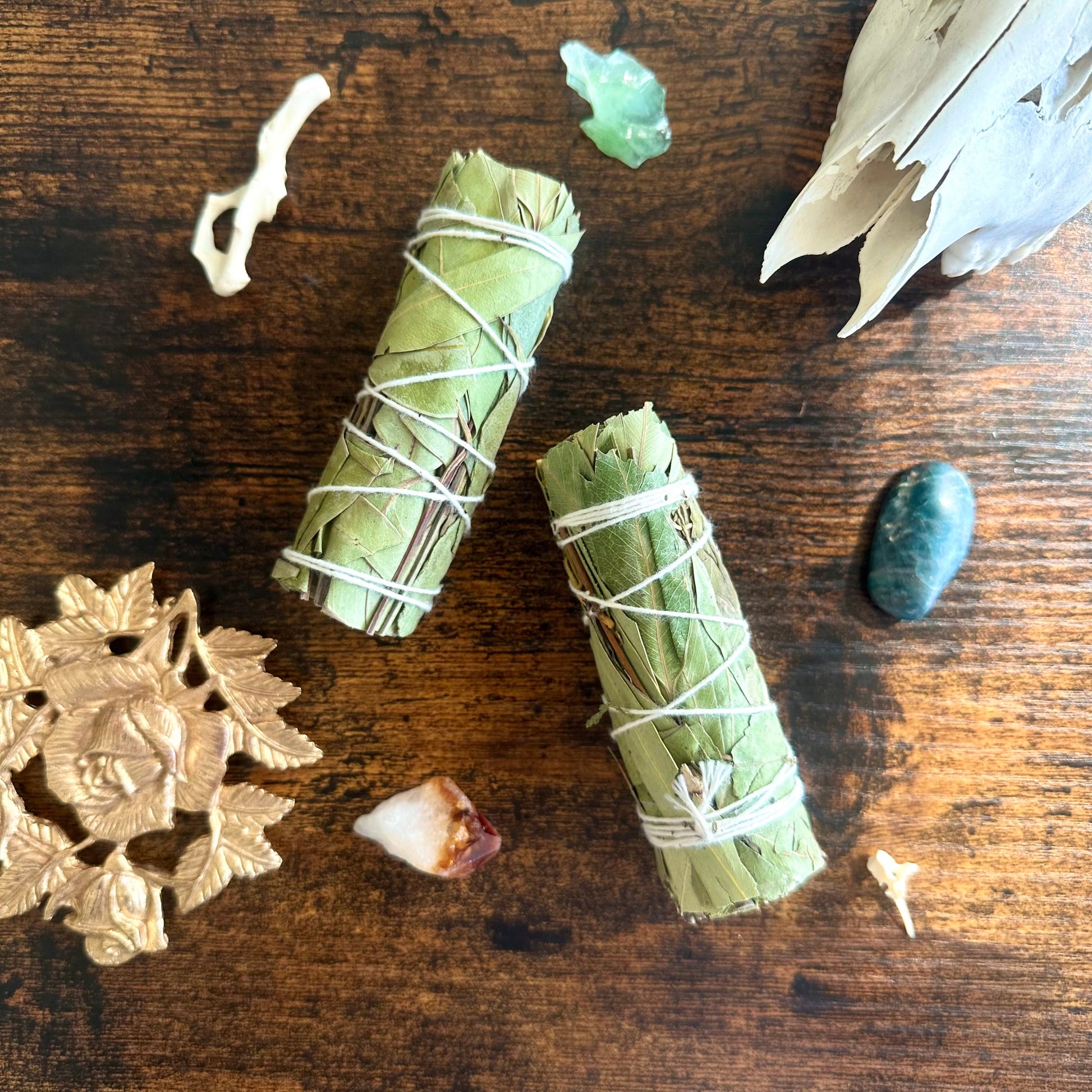 Two green bundles eucalyptus sage wrapped in twine on a wooden surface with decorative elements.