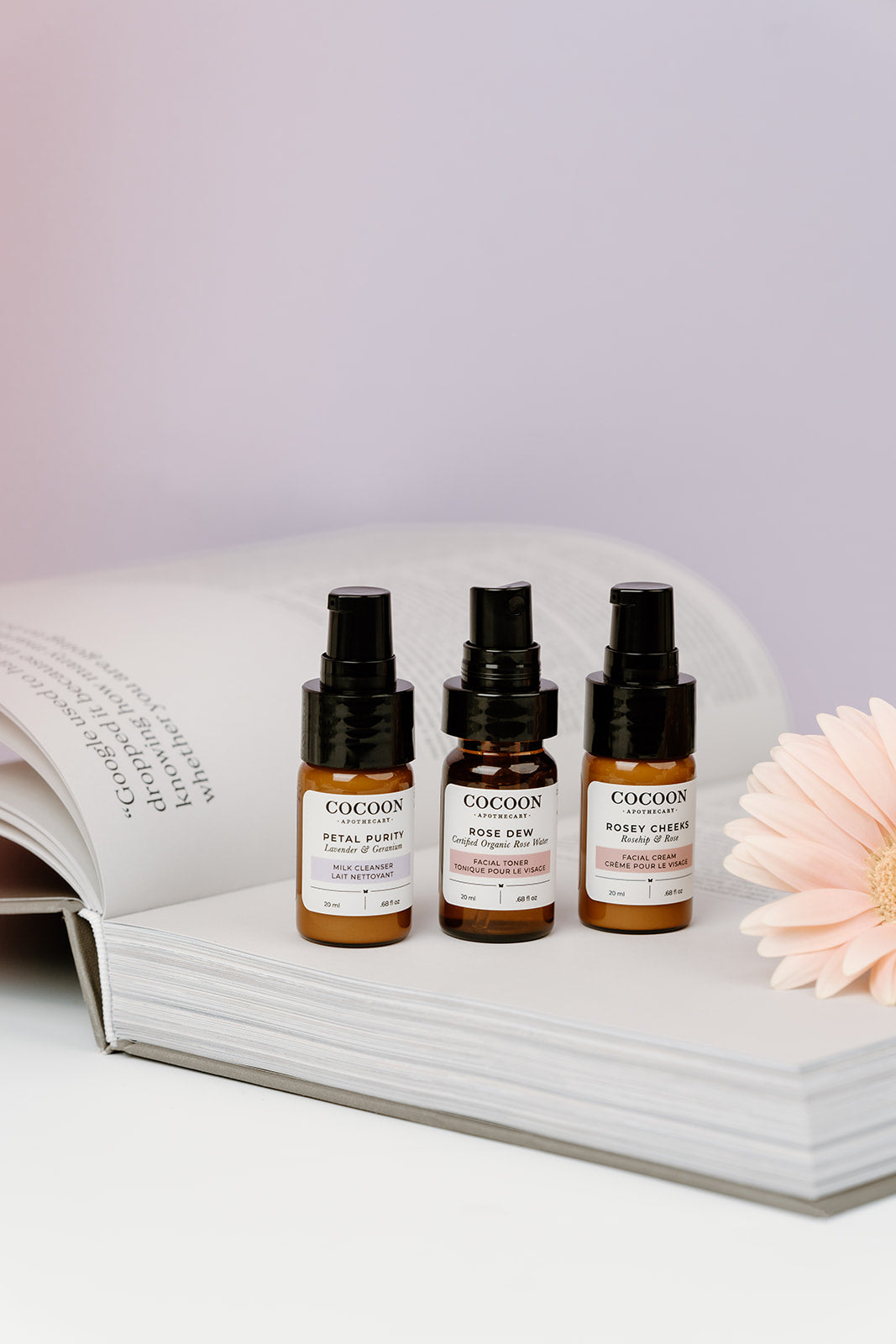 Three small bottles of Cocoon skincare products on an open book with a flower.