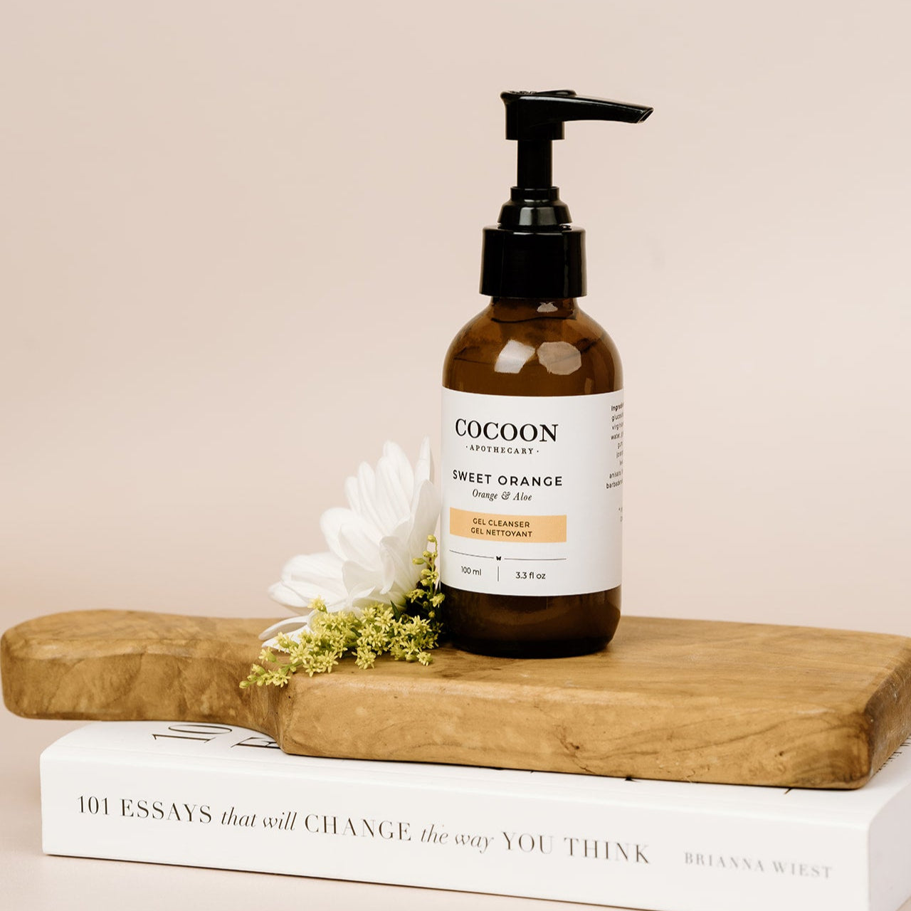 Cocoon skincare bottle of Sweet Orange Gel Cleanser on a wooden block with a book and flowers in the background
