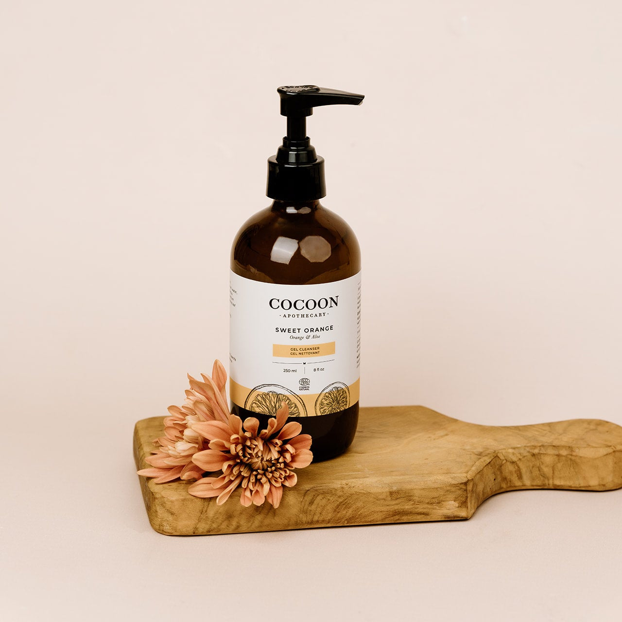 Cocoon Apothecary bottle of Sweet Orange Gel Cleanser on a wooden board with a flower on a beige background