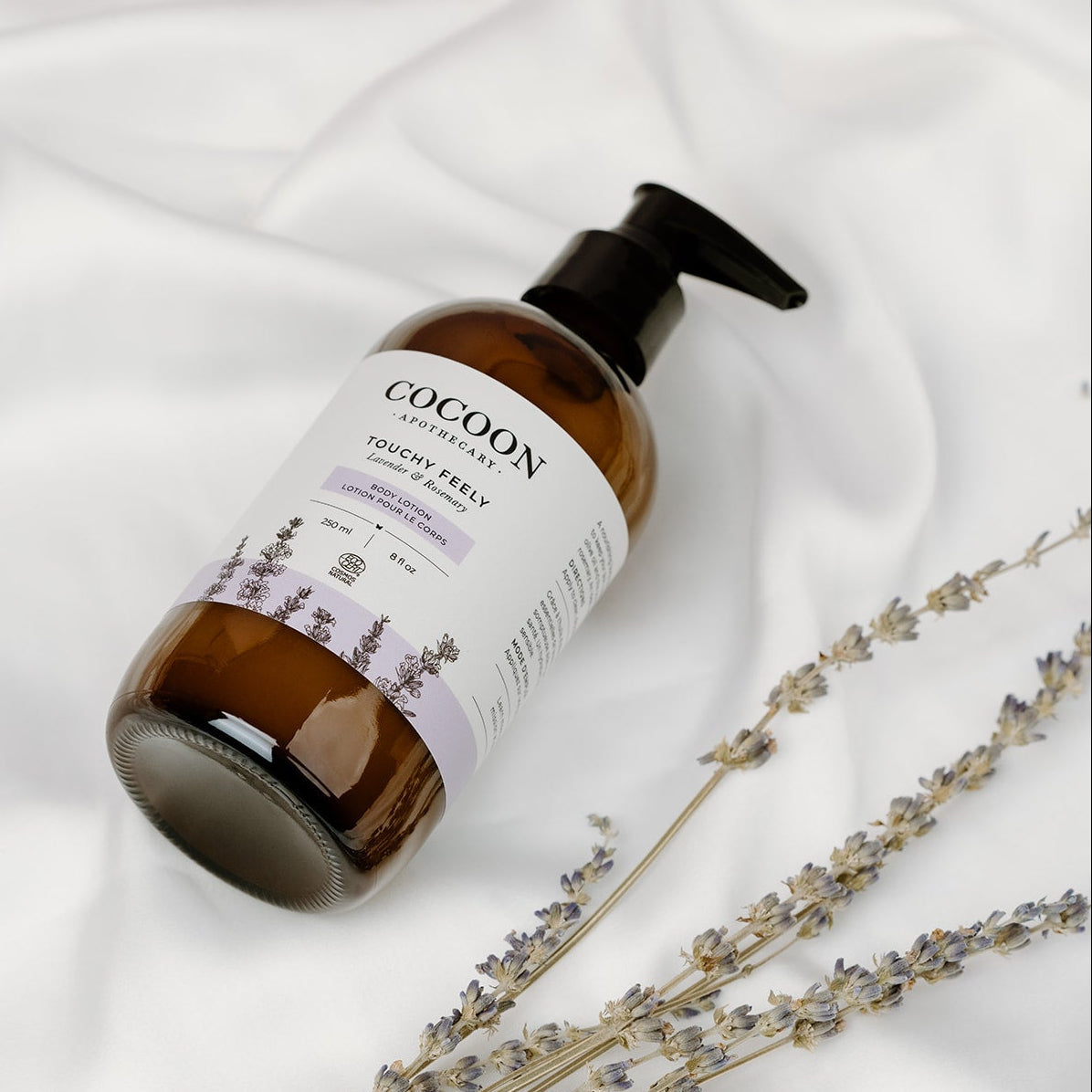 Cocoon Apothecary bottle of Touchy Feely Body Lotion on a white fabric background