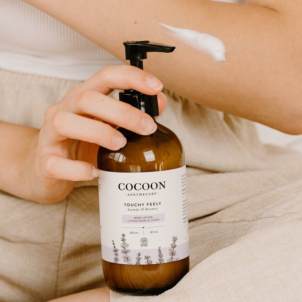 Person holding a bottle of Touchy Feely Body Lotion by Cocoon Apothecary lotion with a blurred background