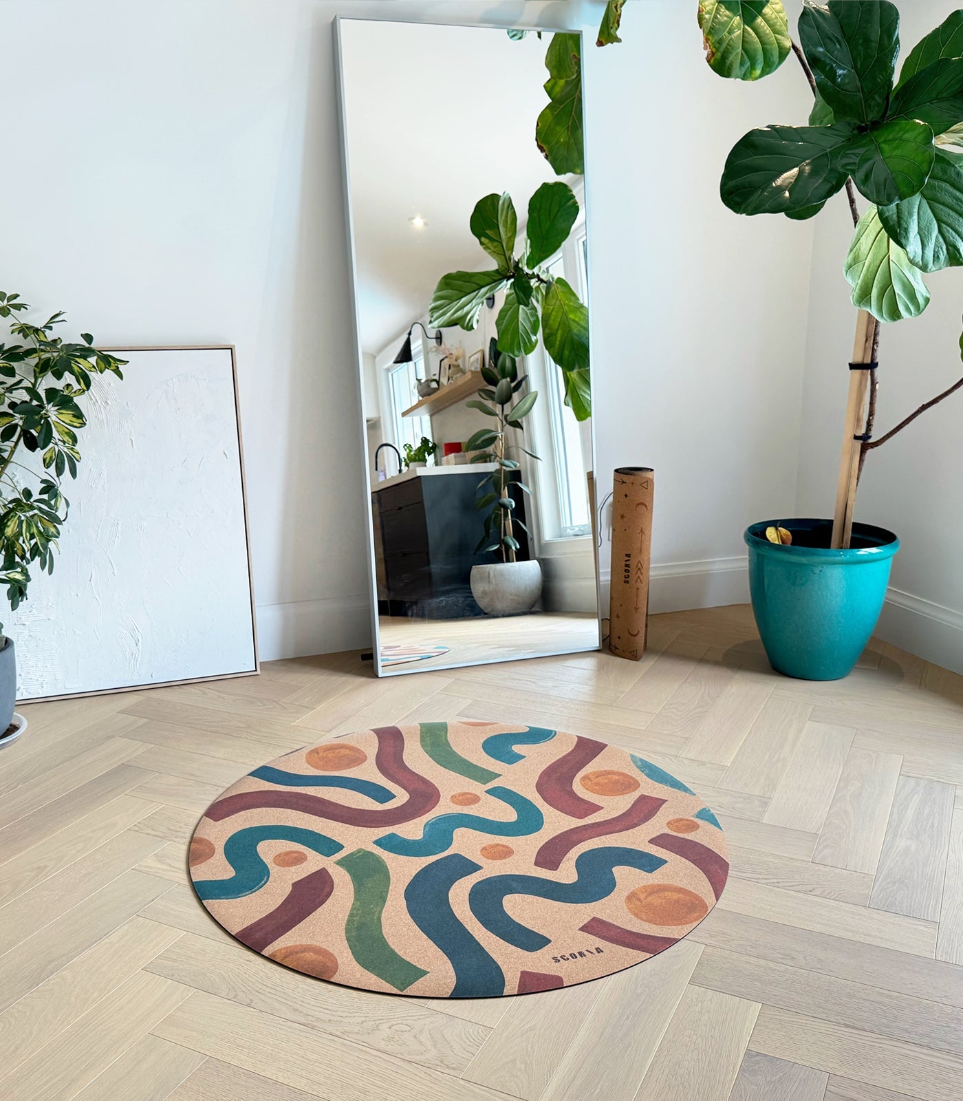 Round colorful cork yoga mat on a wooden floor with a mirror and plants in the background