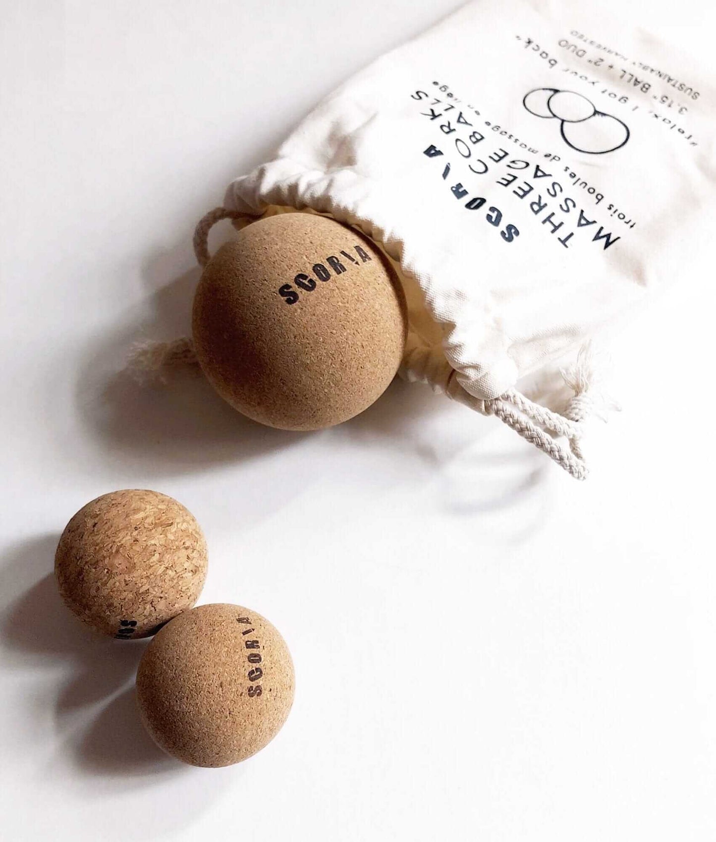 Cork balls with  branding on a white surface, next to a drawstring bag with brand name.