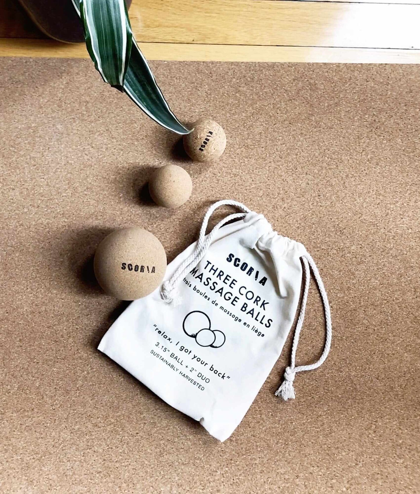 Three cork massage balls with a branded drawstring bag on a wooden surface.