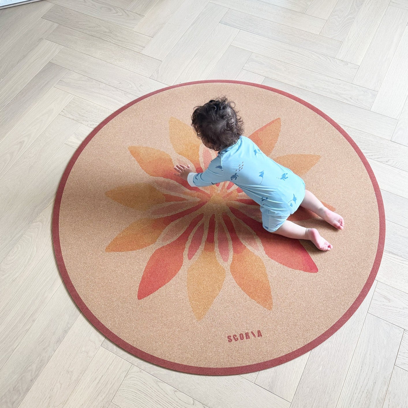 Child playing on a round cork yoga mat with a floral design on a wooden floor