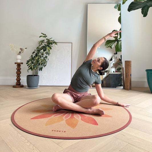woman doing a stretch on a Round cork mat with a floral design in orange and pink in a studio
