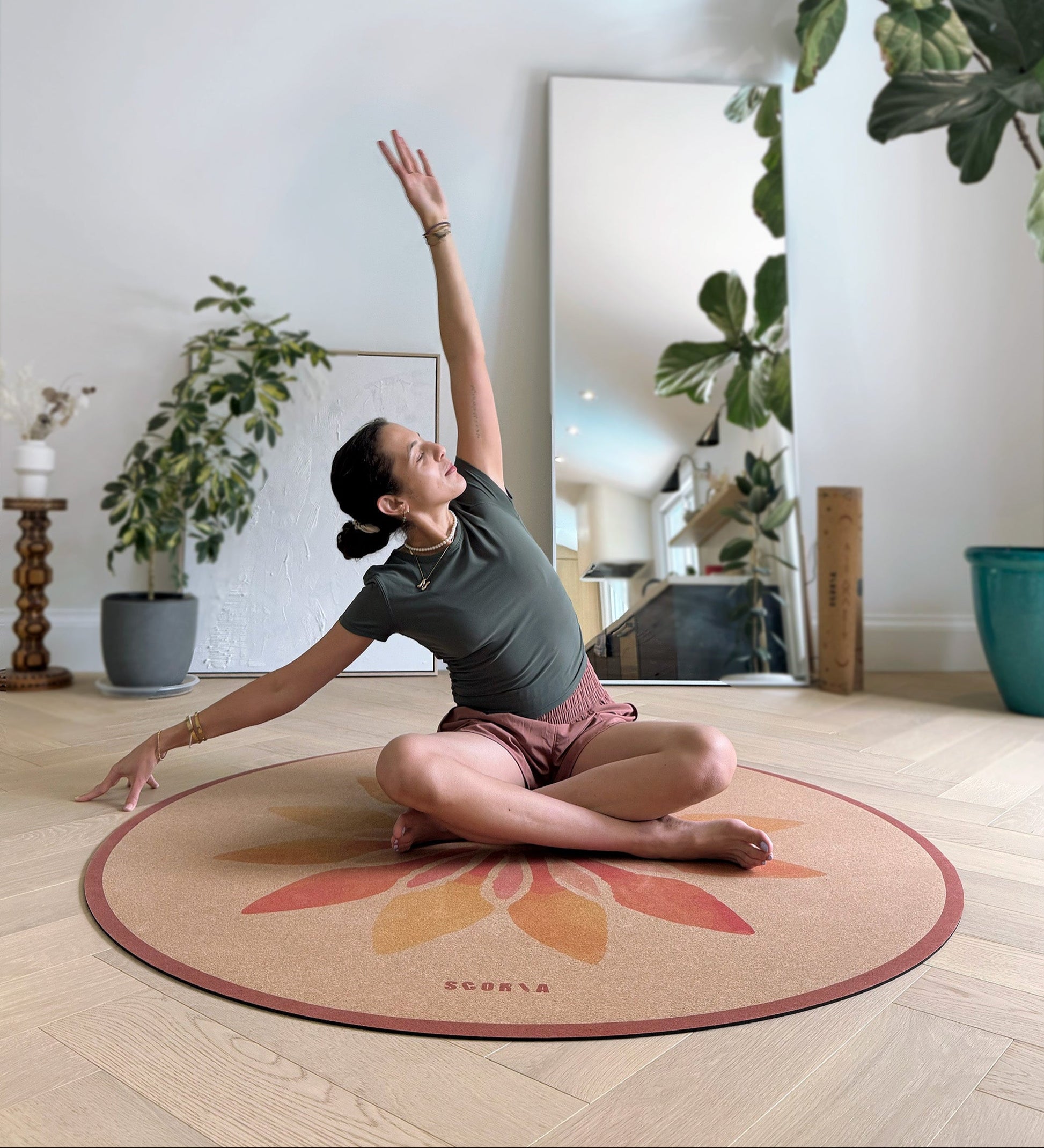 Person practicing yoga on a branded cork mat in a home setting with plants and a mirror.