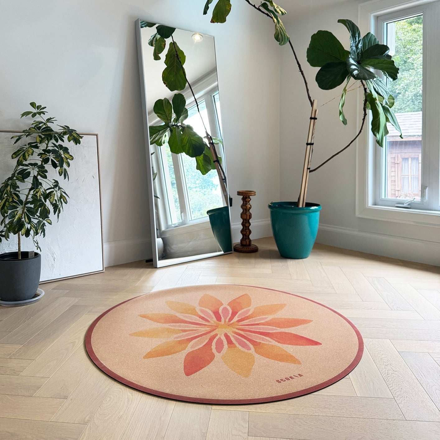 Round floral cork yoga mat on a wooden floor with plants and a mirror in the background