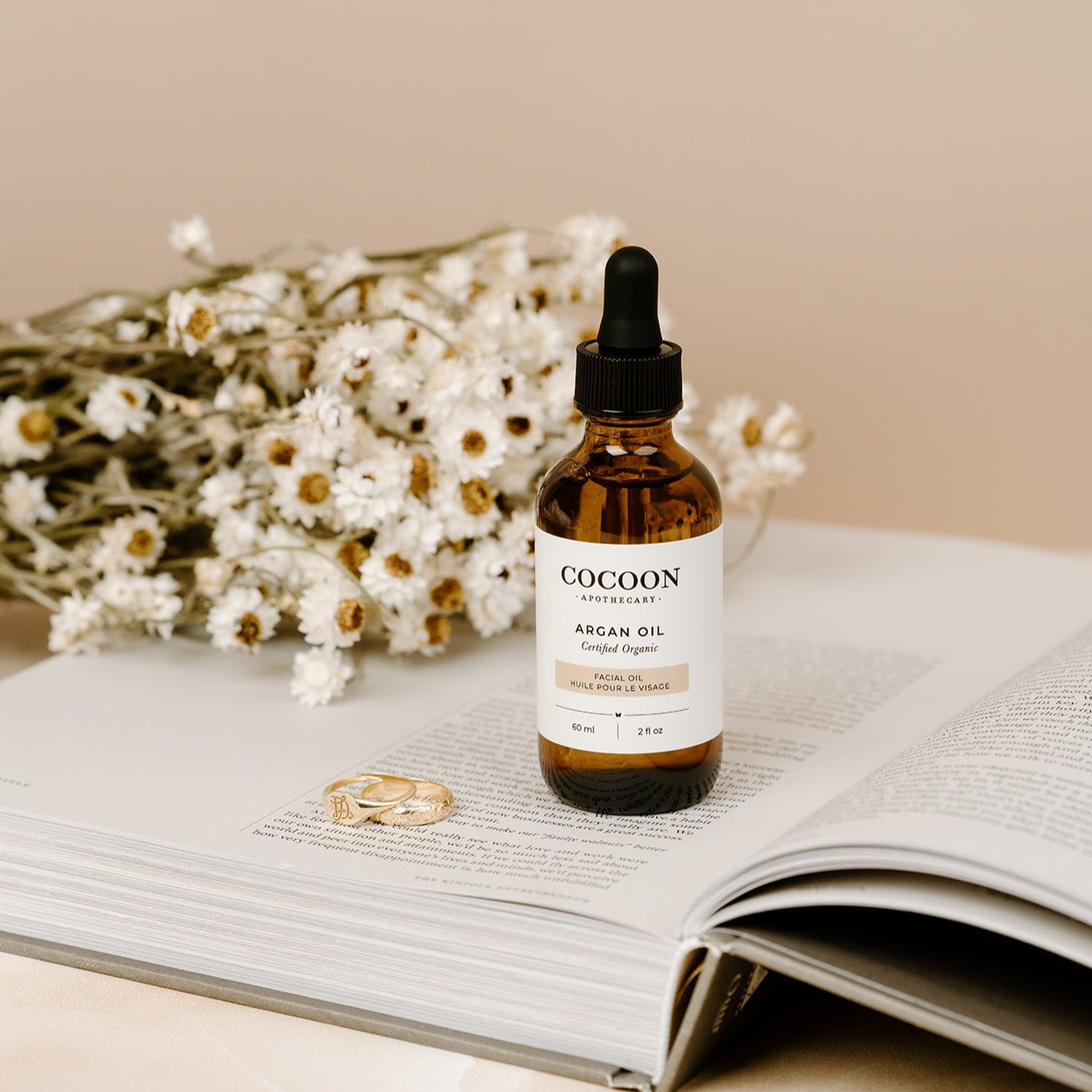 Cocoon Argan Facial Oil bottle on an open book with flowers in the background