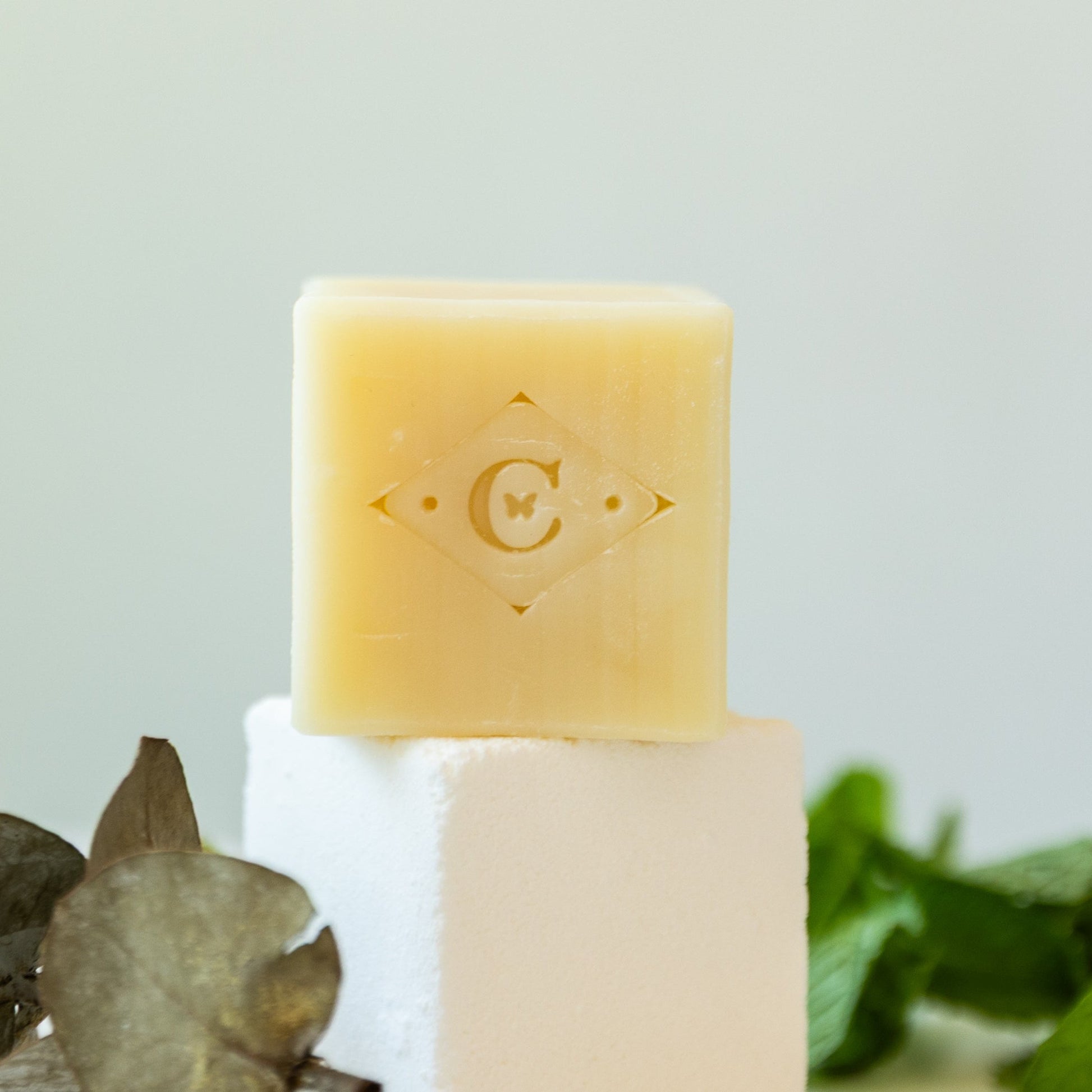 a bar of soap sitting on a bath salt cube with a brand logo on a light background