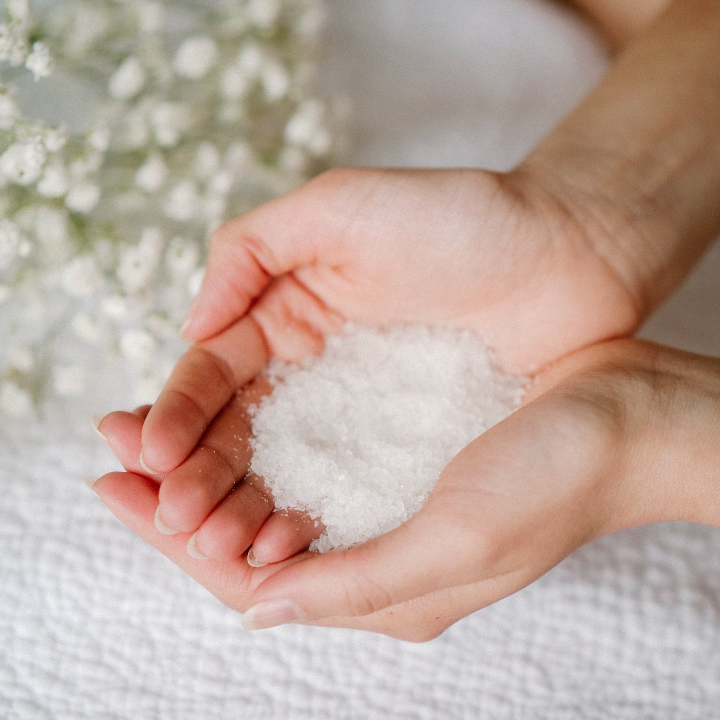 Hands holding a small amount of white Spruce Flora Bath Salts against a blurred natural background
