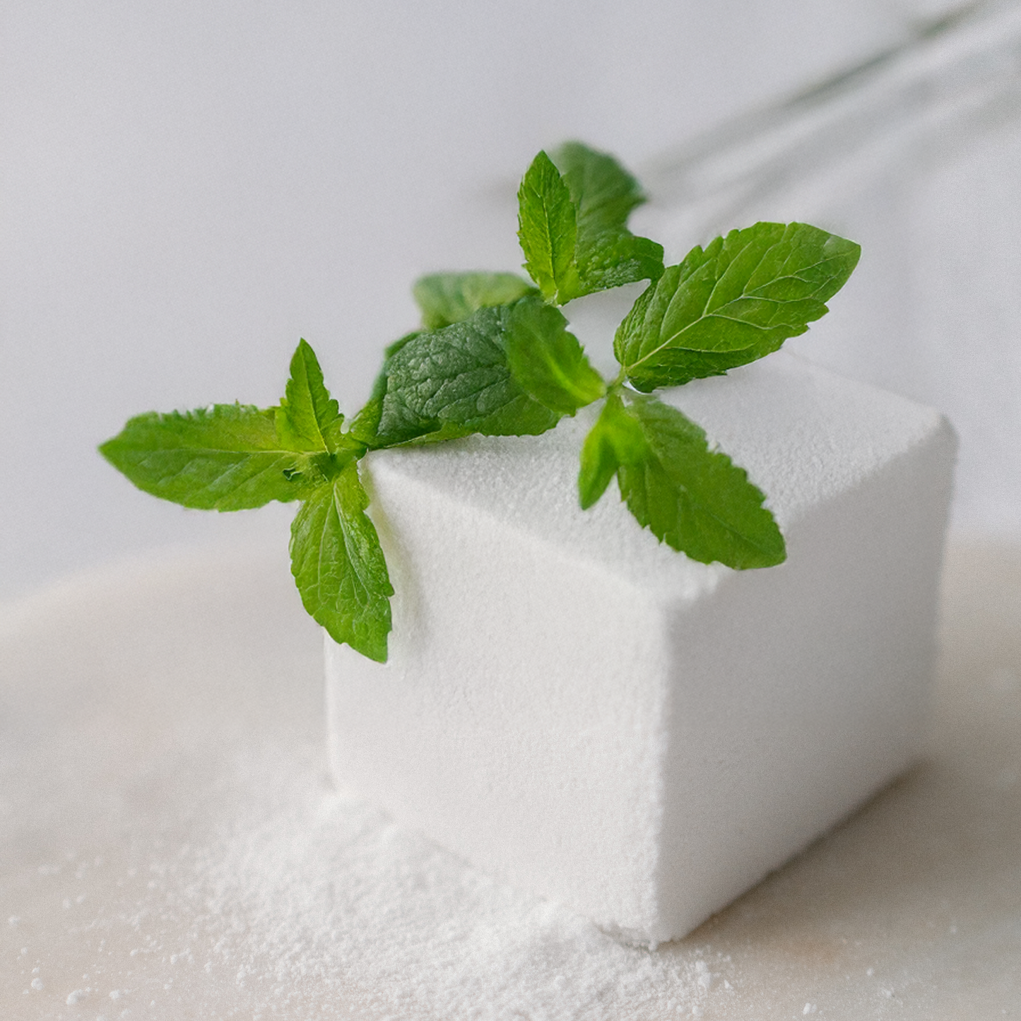 white bath bomb cube with green leaves on a light background