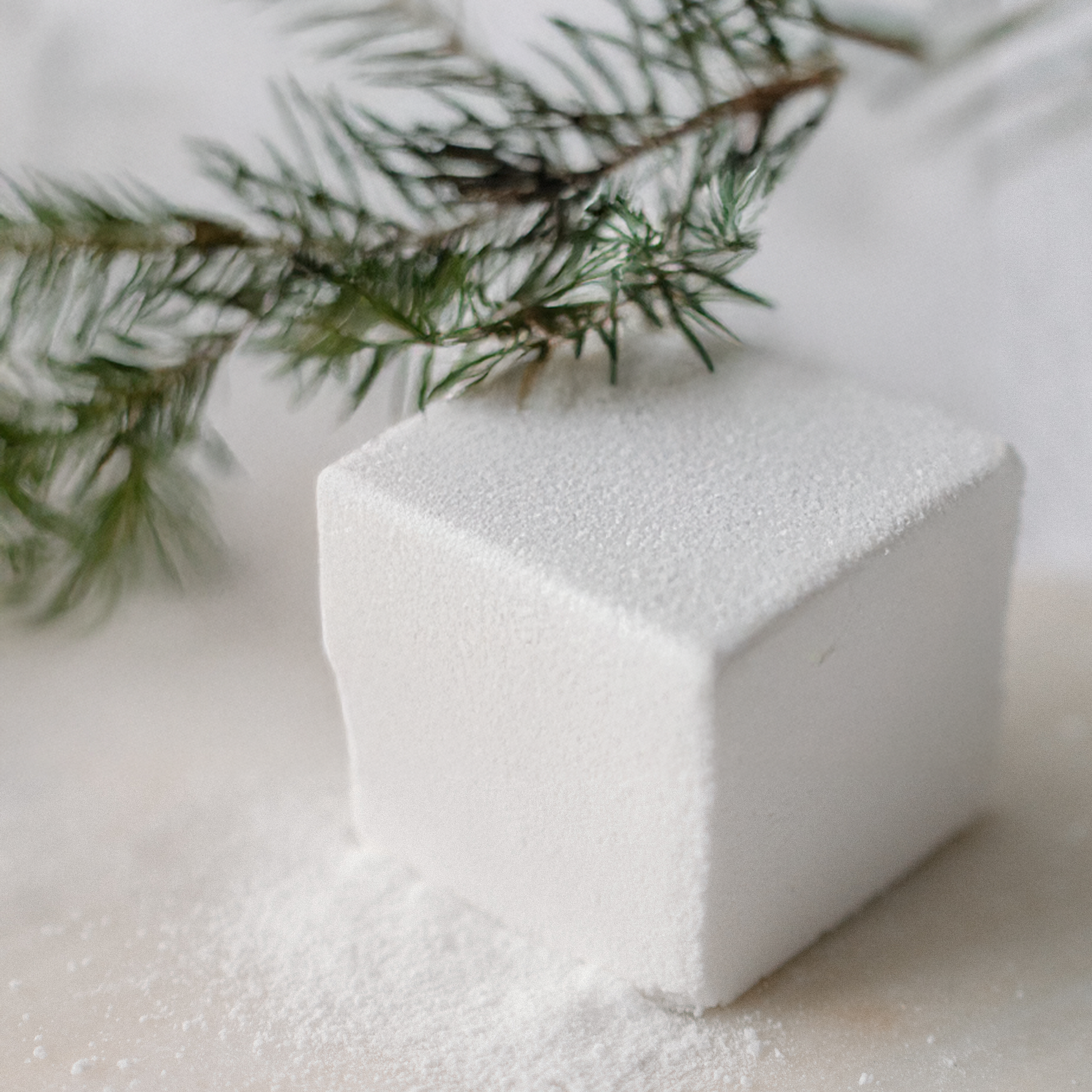 Spruce Flora  Bath Cube on a white surface with a branch in the background
