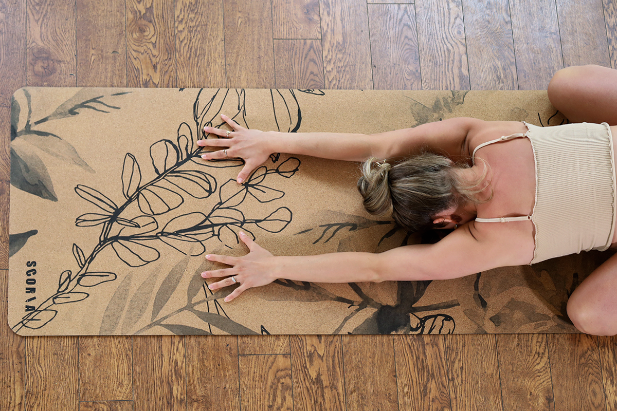 Person stretching on a yoga mat with leaf design on a wooden floor