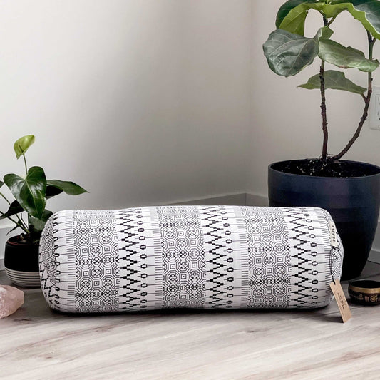 Yoga bolster with geometric pattern on a wooden floor with plants in the background