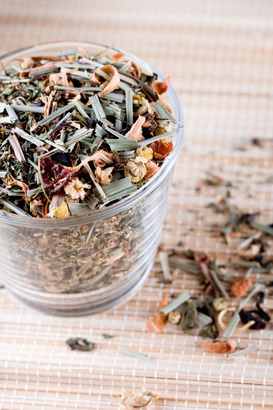 Glass jar filled with a mix of dried herbs for tea on a woven mat