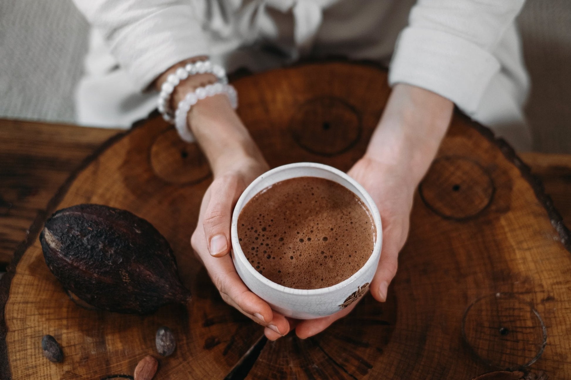 Person holding a cup of changa hot chocolate on a wooden surface with cocoa beans.