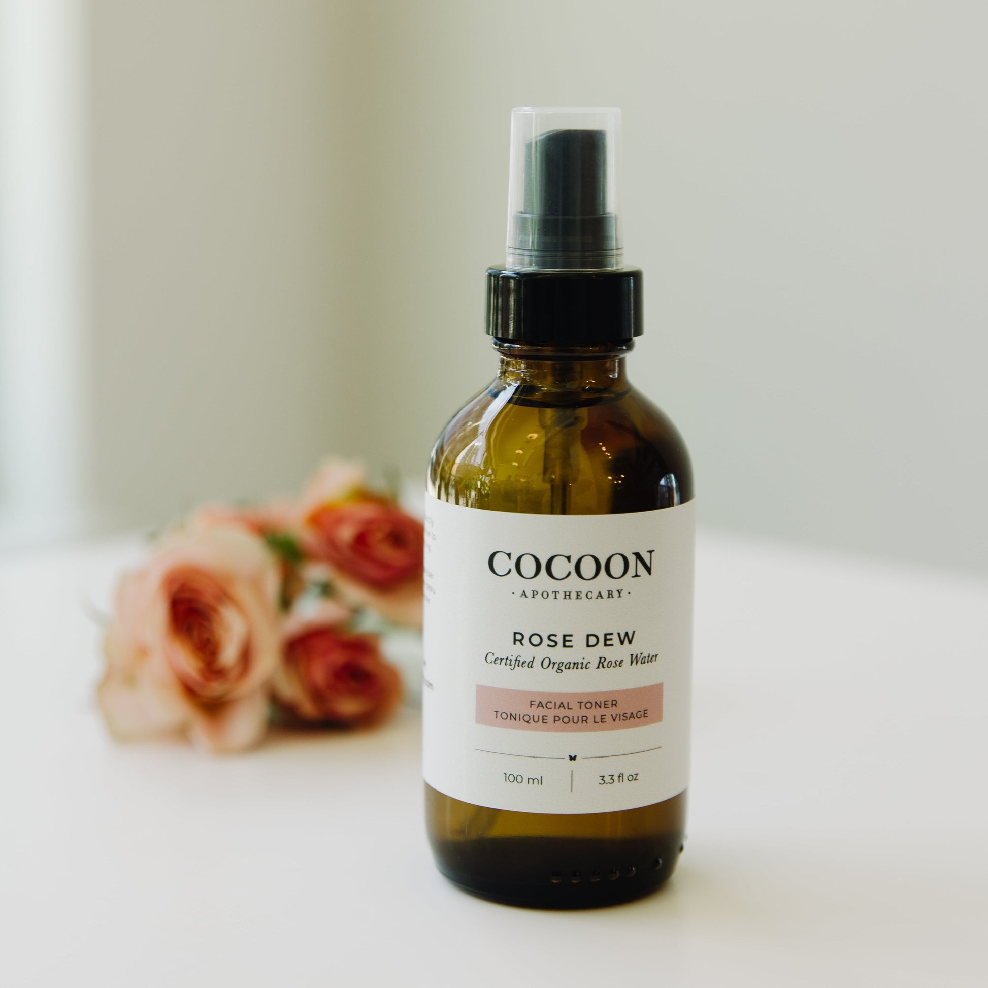 Cocoon Apothecary Rose Dew facial toner bottle with flowers in the background