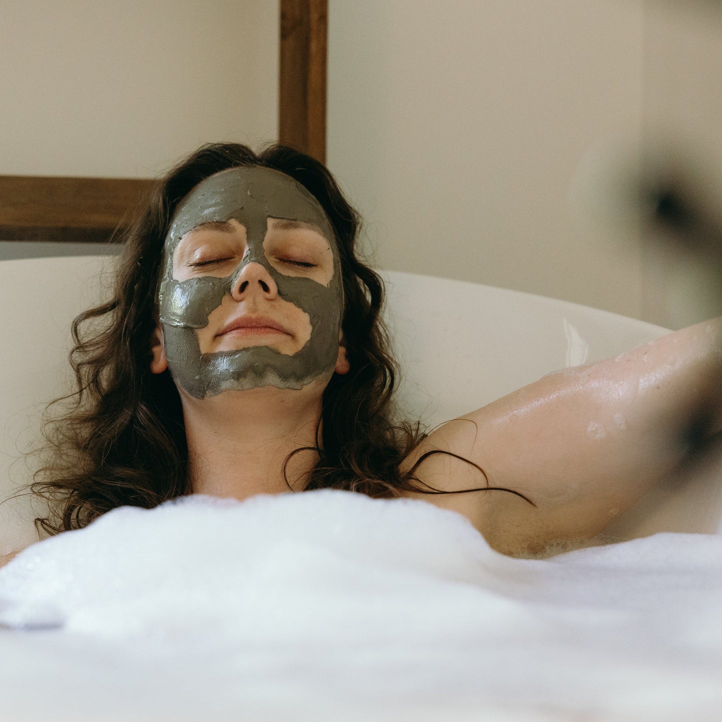 Woman with a mud mask relaxing in a bubble bath