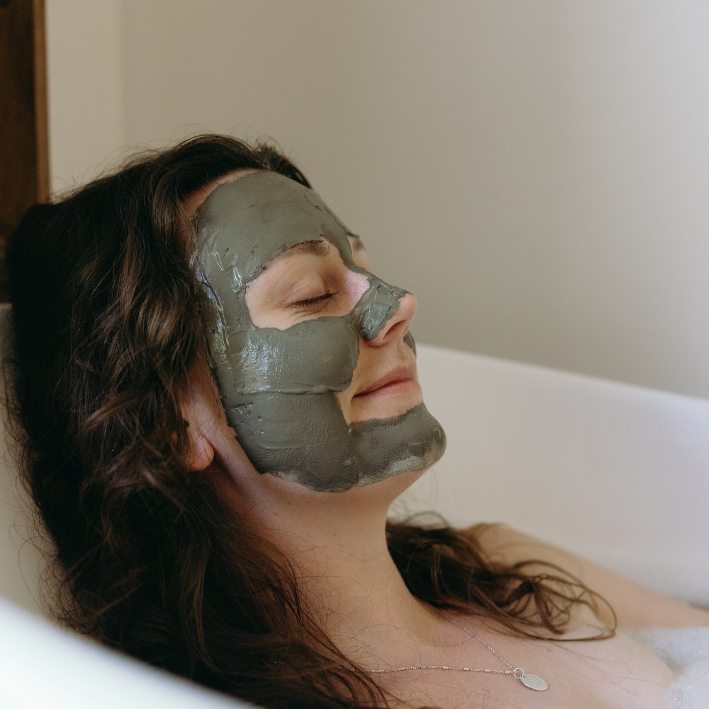 Woman with Ancient Mud Facial Mask on her face lying in a bathtub
