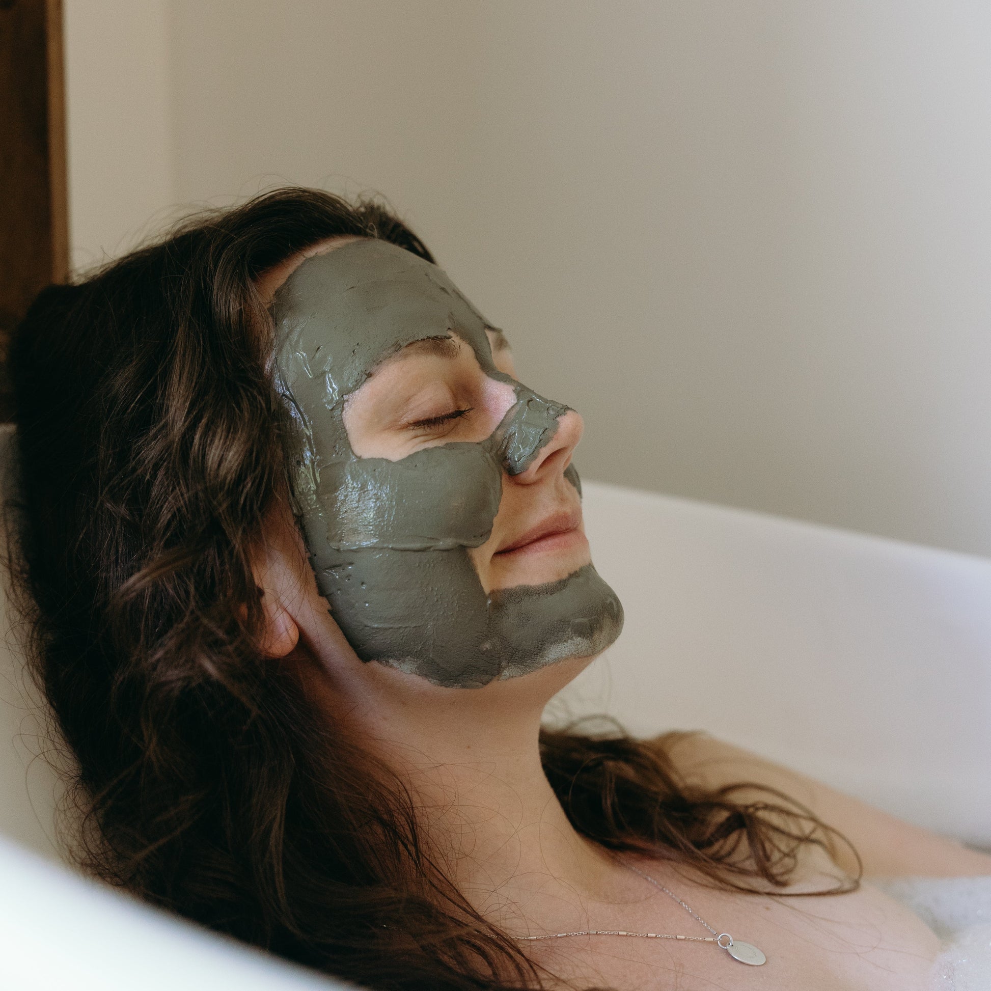 Woman with Ancient Mud Facial Mask on her face lying in a bathtub