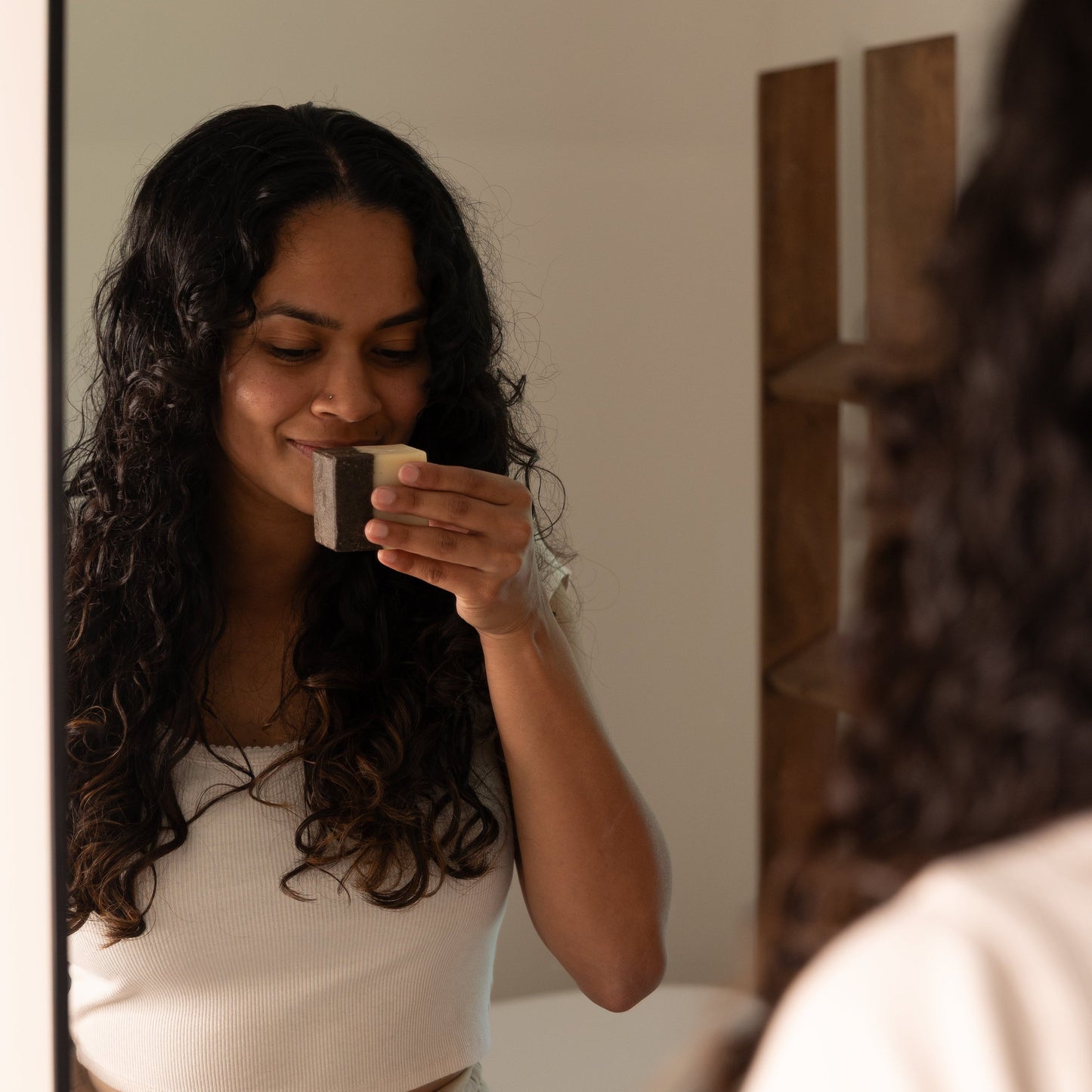 Woman holding Coffee Scrub Bar Soap in front of her nose in front of a mirror