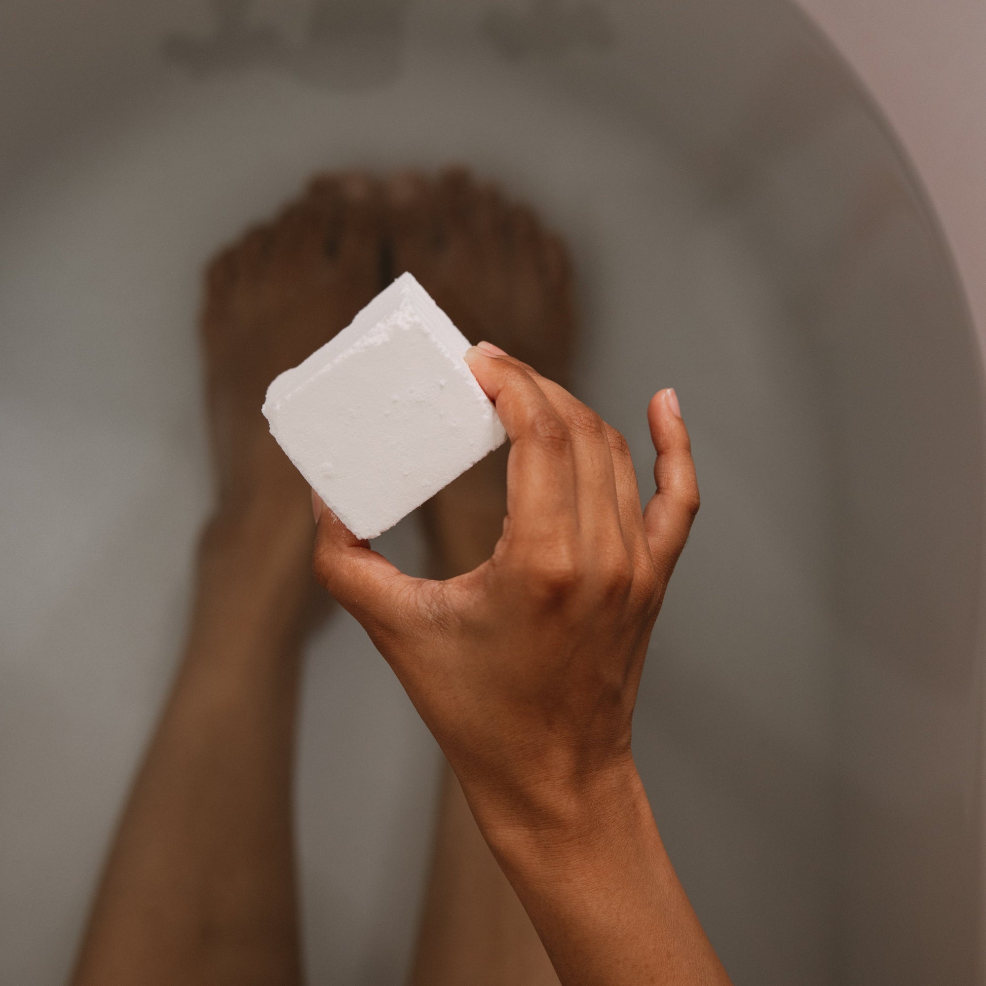Hand holding a Citrus Tea bath cube above a bathtub