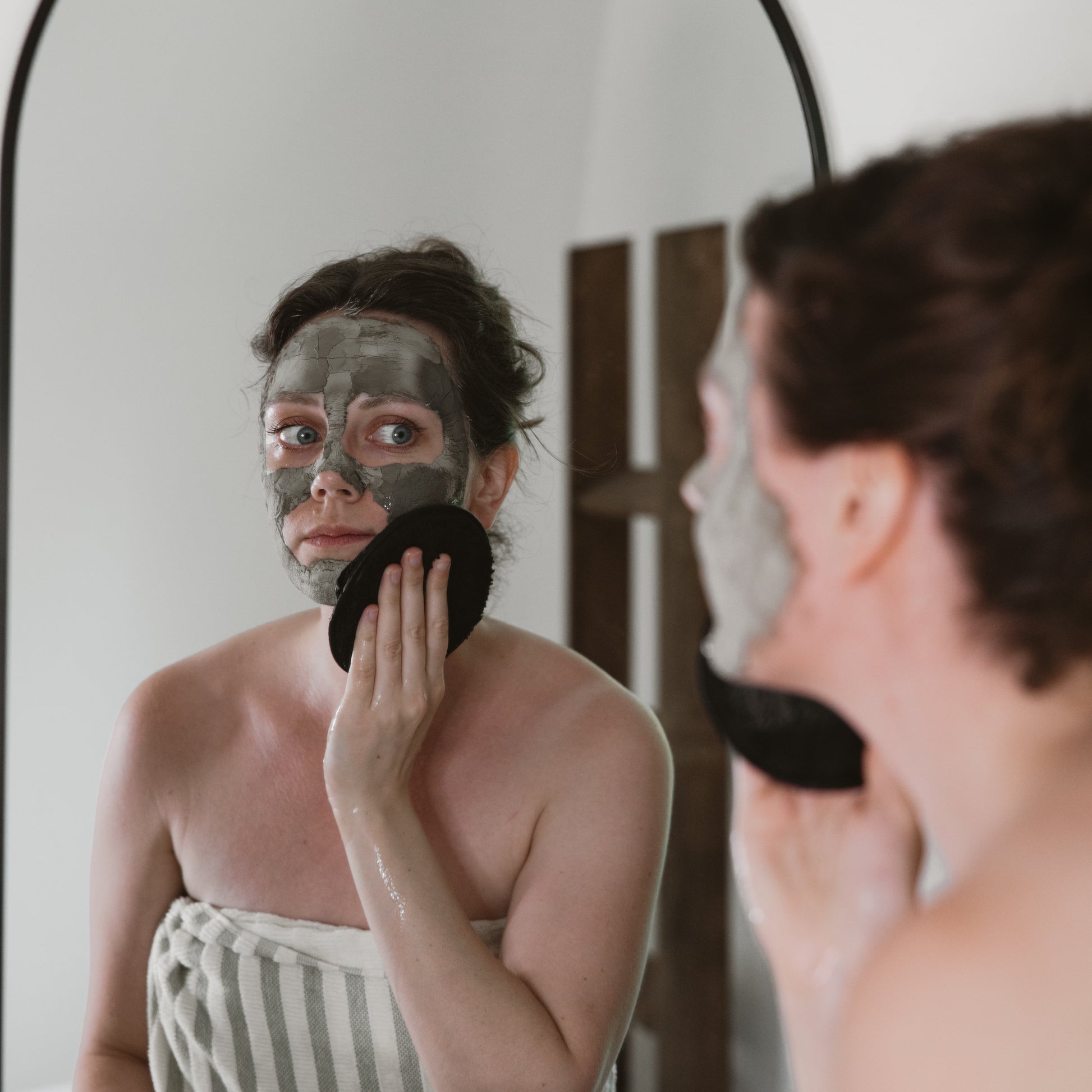 Person applying a Ancient Mud Facial Mask in front of a mirror