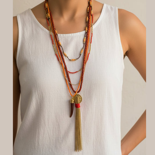 Dramatic multi-strand boho necklace with red and orange braided leather, seed bead strands, gold ball chain, wood tube beads, gold coin pendant, dark wood drop and long gold chain tassel worn by a woman — handmade in India for bold bohemian and statement style