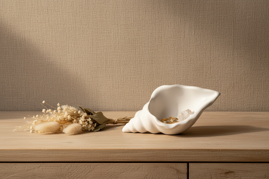 Matte white conch shell shaped jesmonite trinket tray and jewelry dish styled on a bedroom dresser with gold rings, crystals, and dried florals in warm natural light