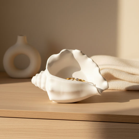 Matte white conch shell shaped jesmonite trinket tray and jewelry dish with gold rings on a bedroom dresser in warm natural light