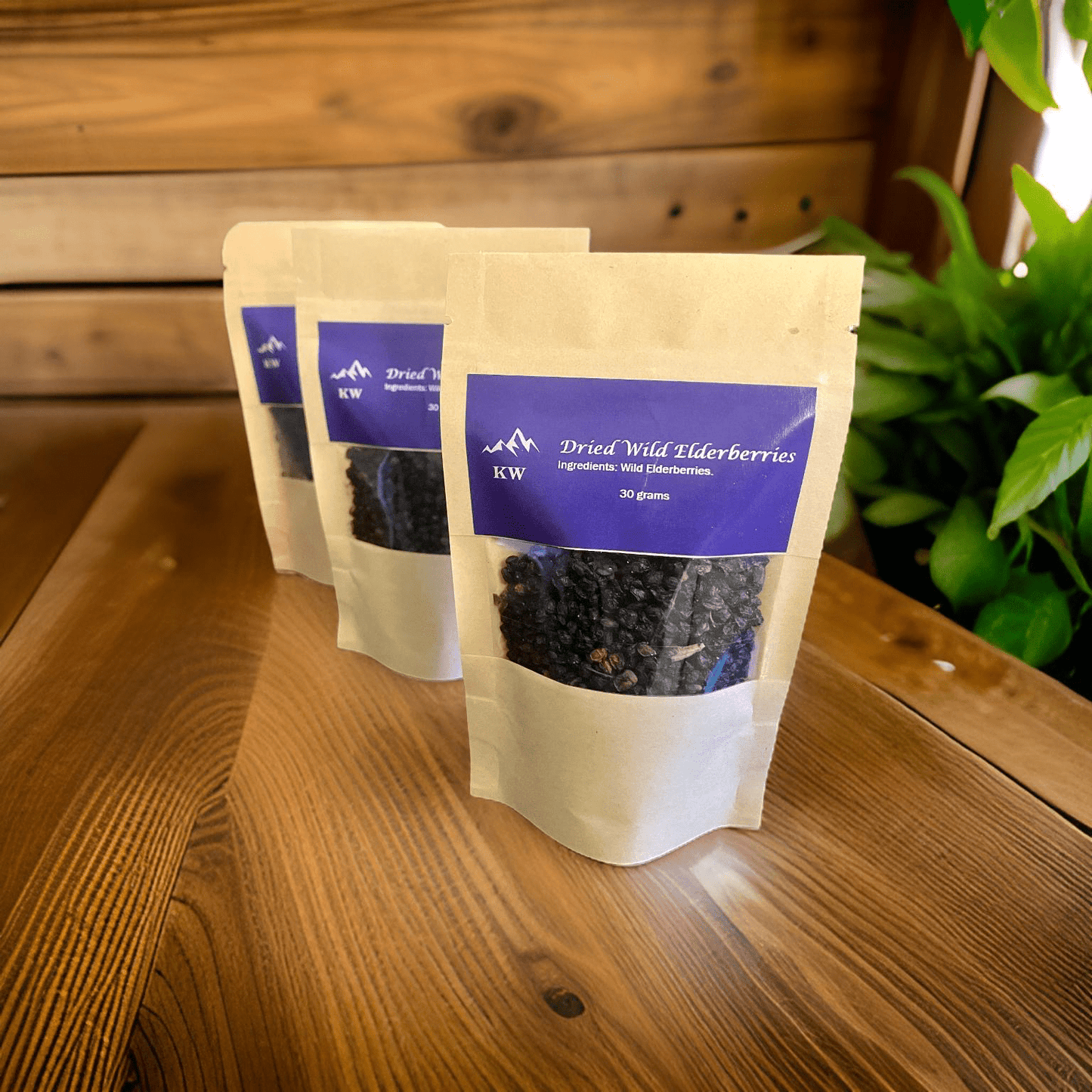 Three bags of dried wild elderberries on a wooden surface with a plant in the background.